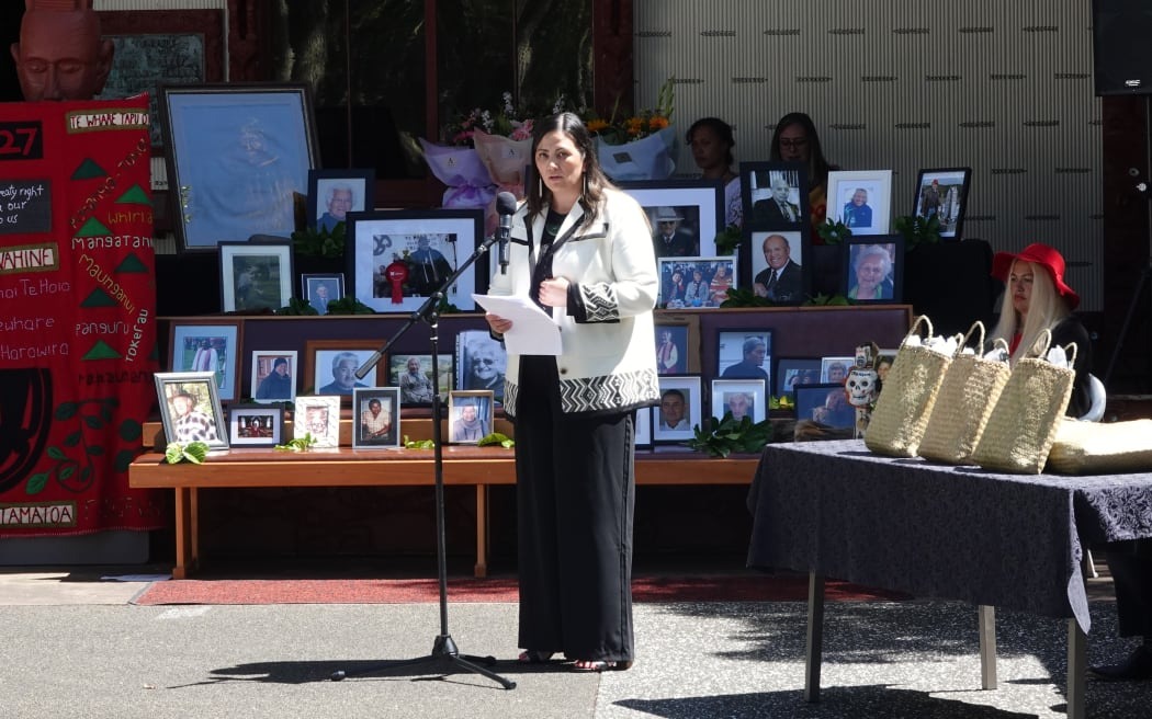 Waitangi Tribunal deputy director Sandra Edmonds reads a summary of the report, in front of photos of Tribunal members and claimants who did not live to see the final report are displayed on the porch of Te Whare Rūnanga.