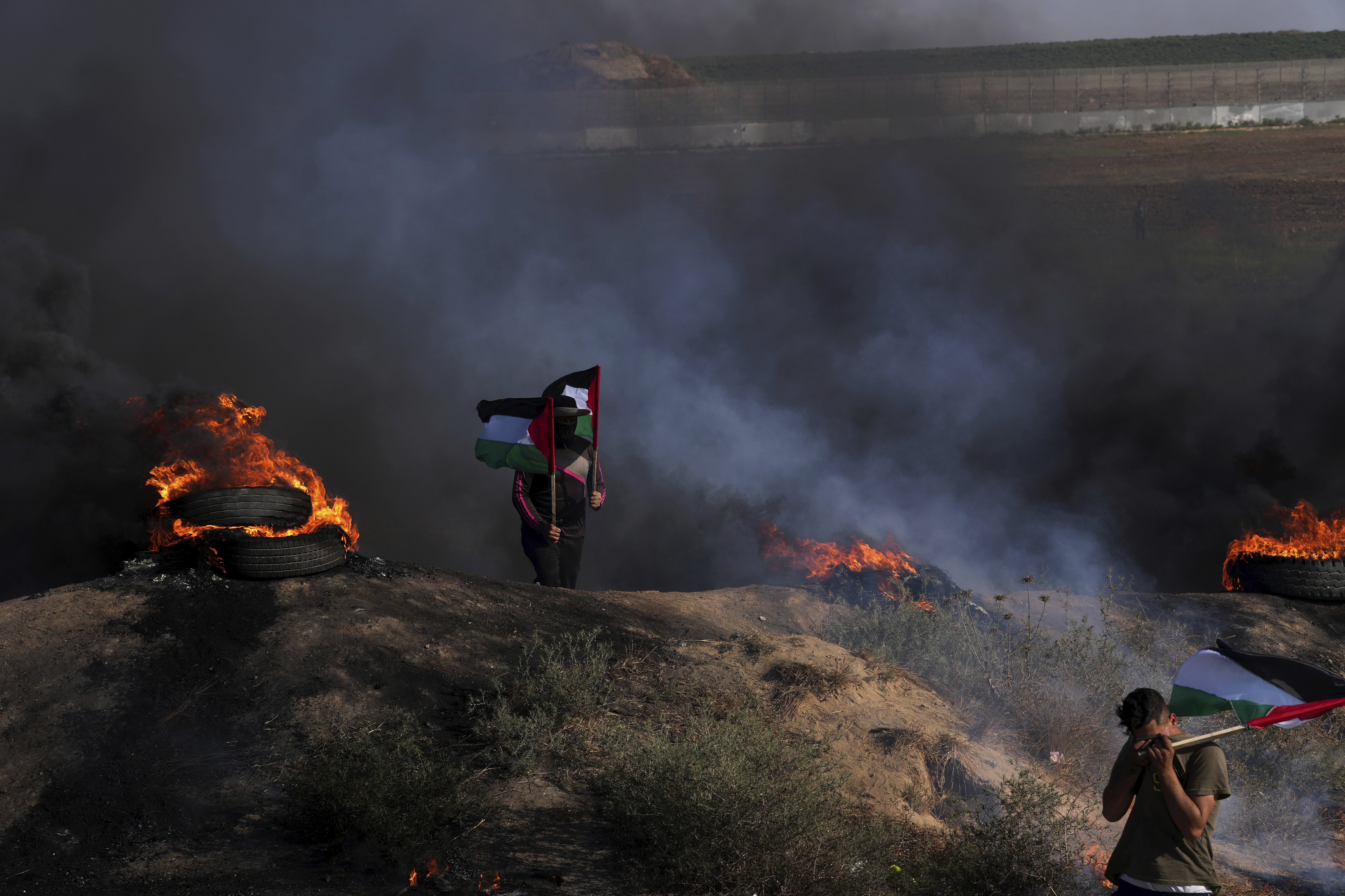 Palestinian demonstrators wave their national flags while others burn tyres during a protest against an Israeli military raid. Photo / AP
