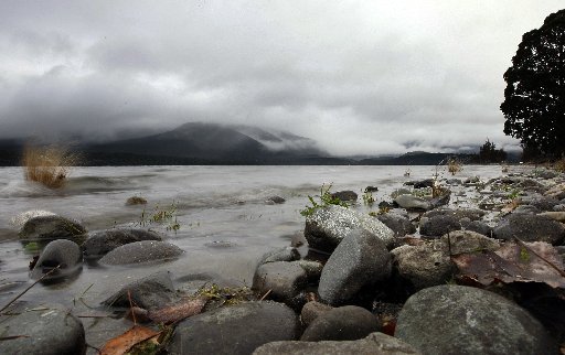 Lake Te Anau laps at the shore, with mist on the mountains around it.