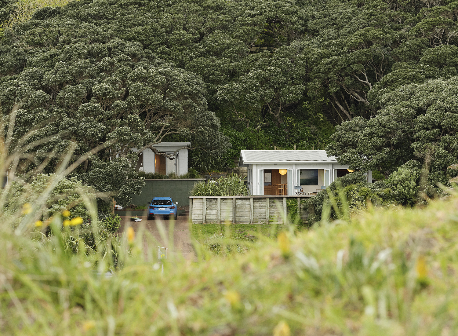 Ngahuia and Steve’s Piha bach nestles into the foot of the hill, surrounded by established pōhutukawa trees. Photo / Derek Henderson
