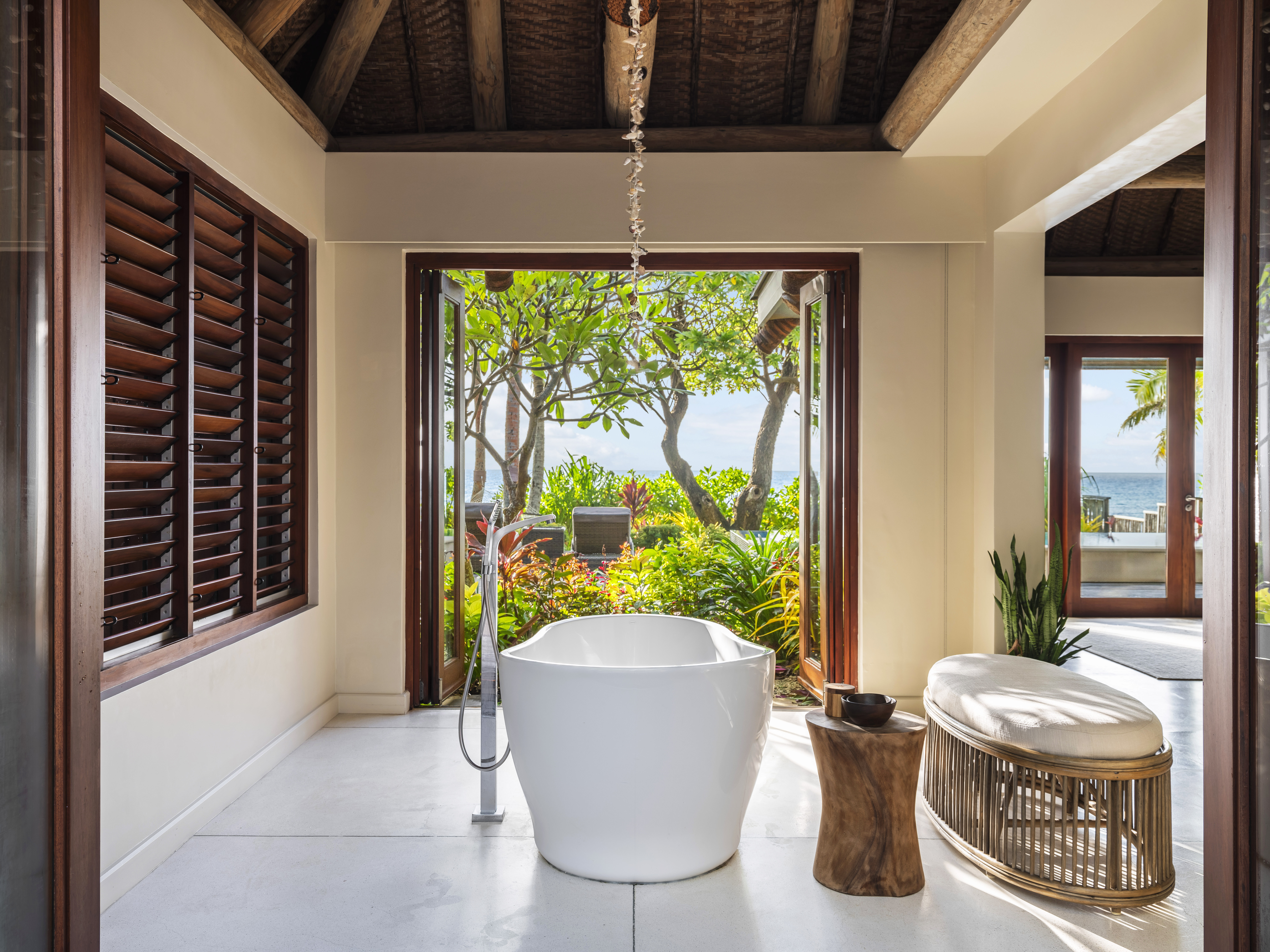 Luxurious bathroom features marble tub opening to tropical garden views.