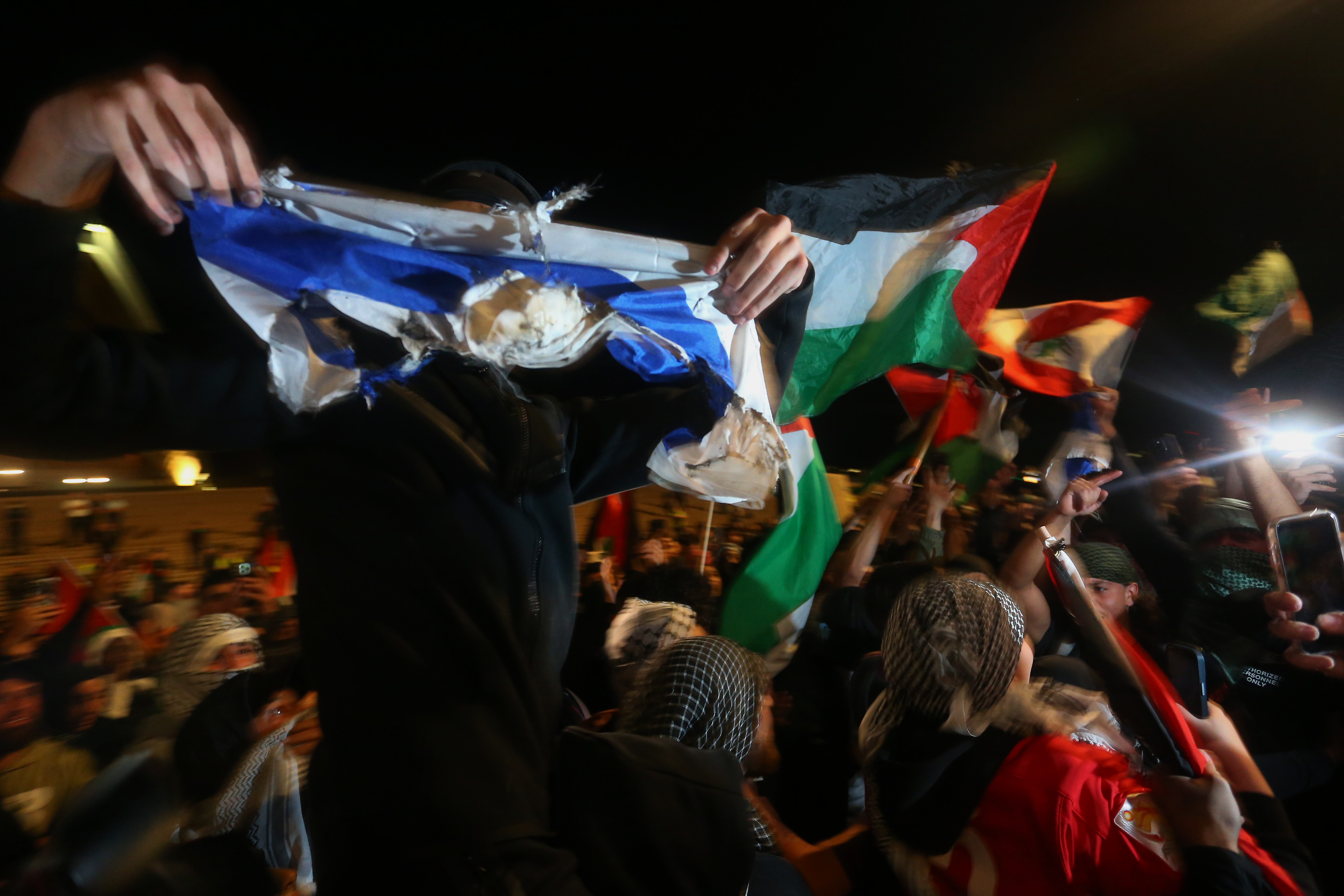A Palestine supporter holds a burned Israeli flag in the air during a rally outside the Sydney Opera House. Photo / Getty Images