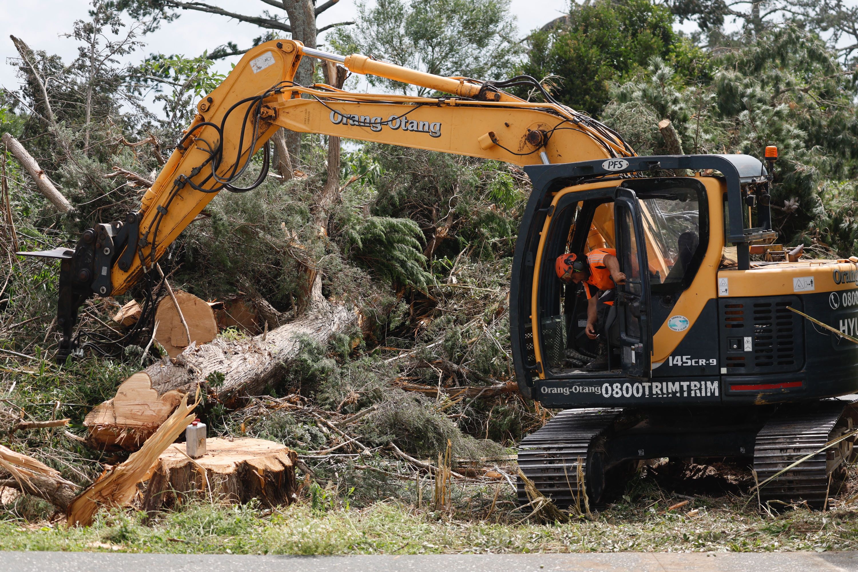 A digger operator at work clearing fallen trees a day a tornado ripped through the beach settlement of Mangawhai, north of Auckland. Photo / Michael Craig