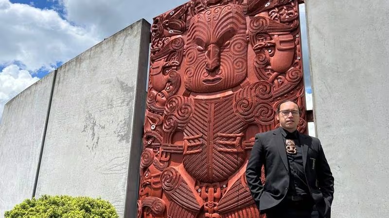 Newly-appointed Tumu Whakairo Rākau Grant Marunui stands by a tōtara pou whakairo - one of three he led in design - showcasing the Ngāti Whakaue style, reflecting his iwi, at NZMACI’s entrance.