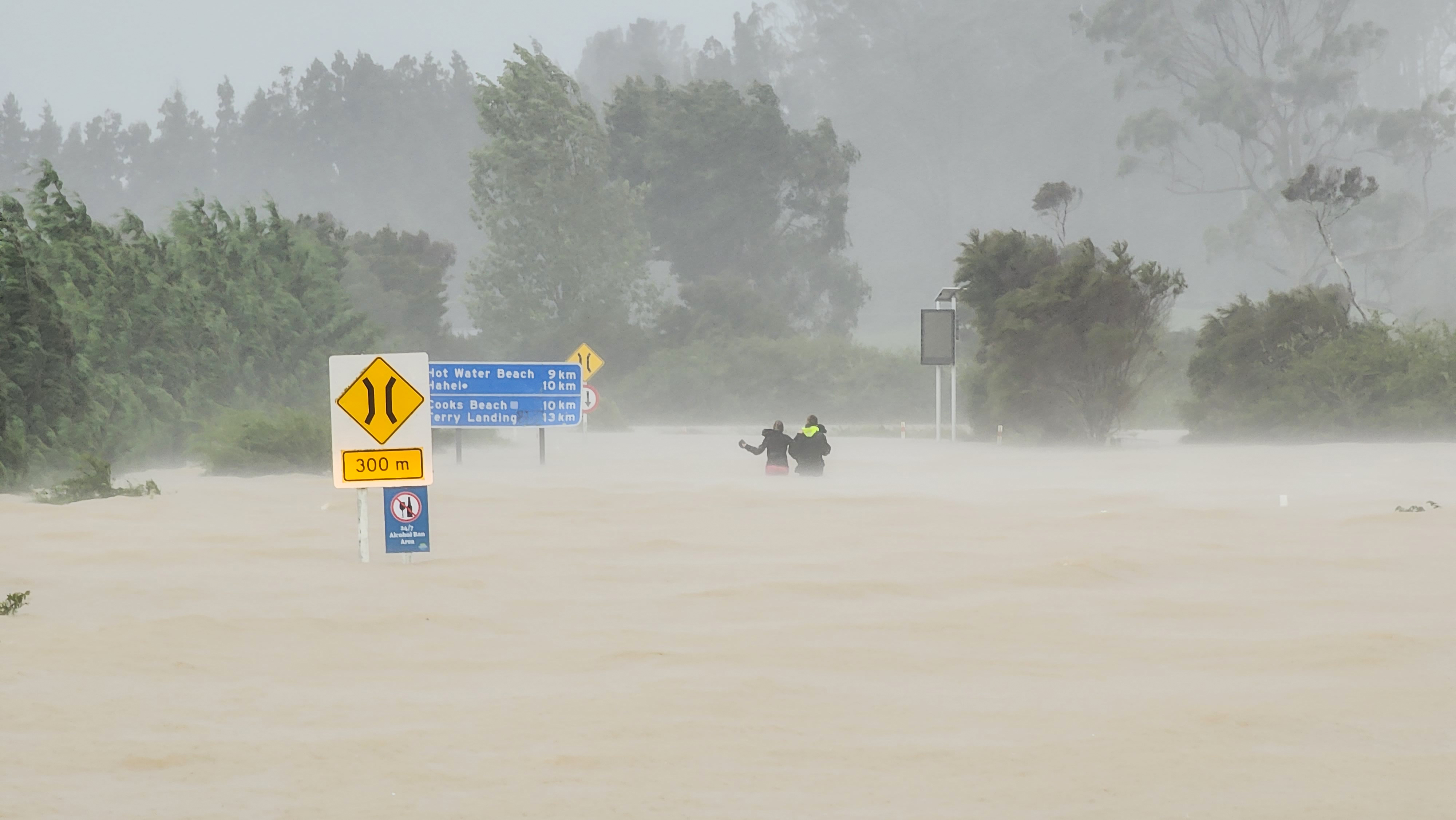 Two people wade through waist-high water after abandoning their car on the road to Hahei on the Coromandel Peninsula as Cyclone Gabrielle brings extreme weather to New Zealand. Photo / Matthew Davidson
