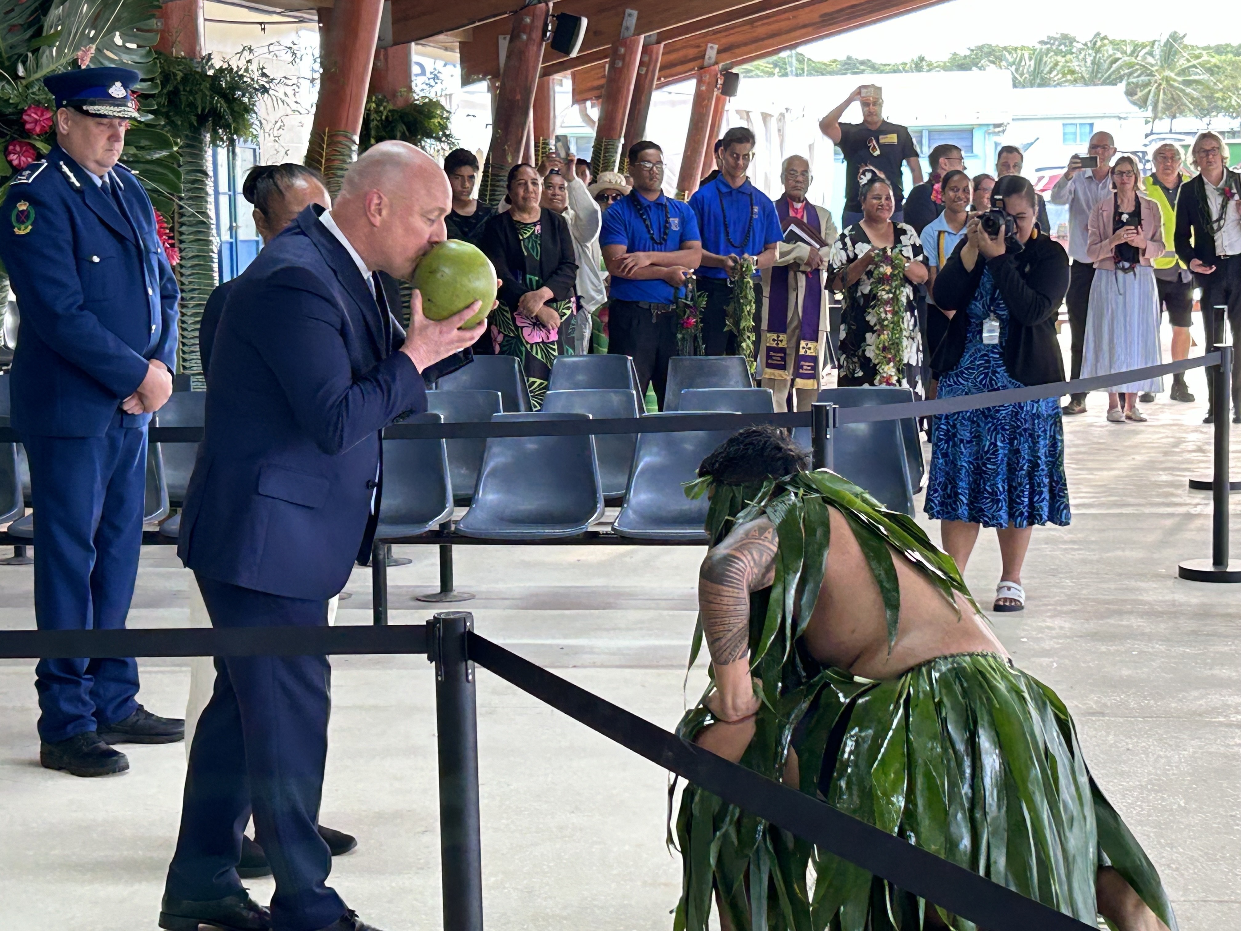 A warrior kneels before Prime Minister Christopher Luxon after presenting him with a pierced coconut, from which Luxon drinks as he is welcomed to Niue. Photo / Adam Pearse