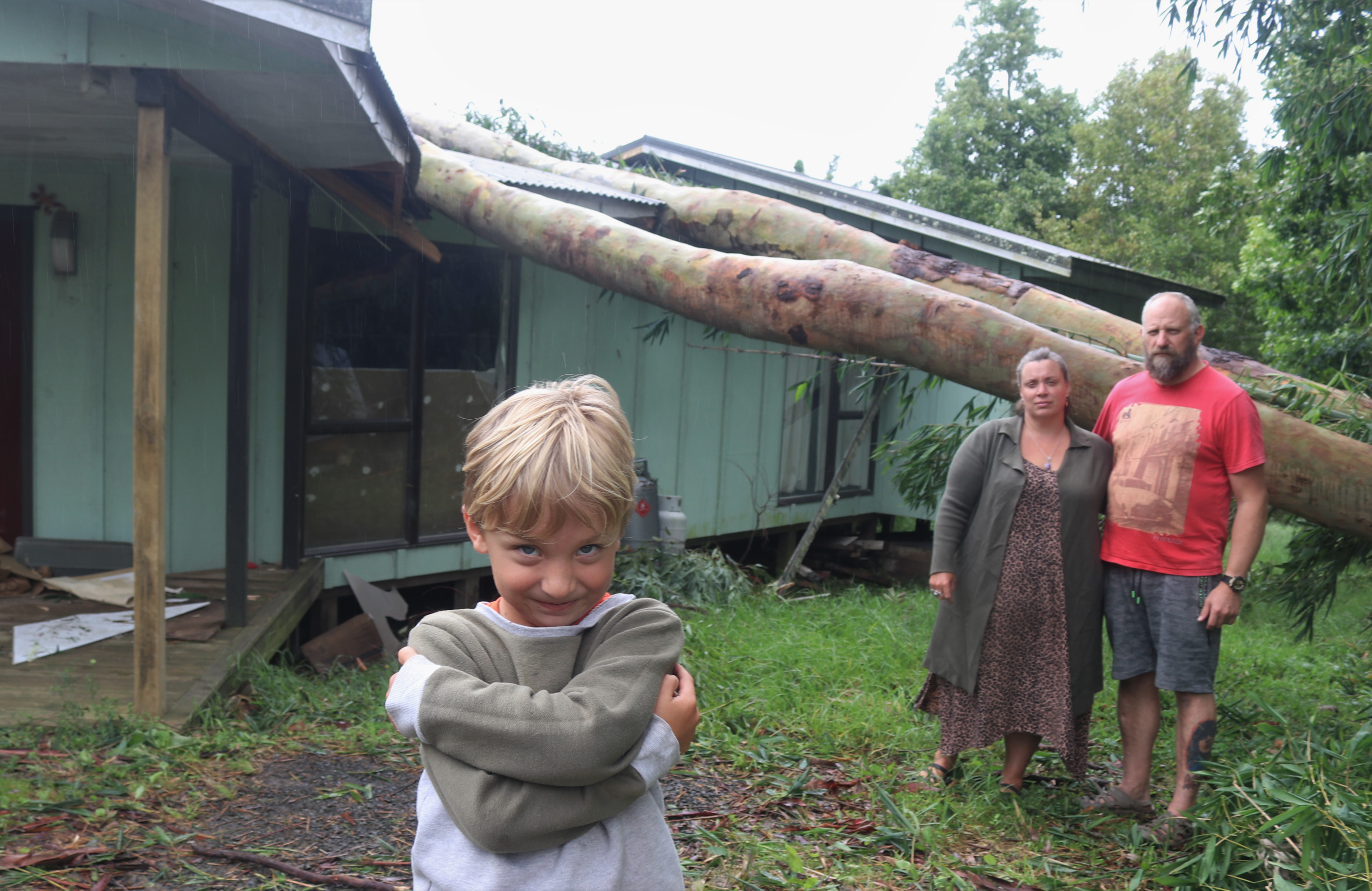 Ashton Edwards, six, with his parents Tane and Monique and the gum trees Cyclone Gabrielle pulled down on to their Waipapa home in February.