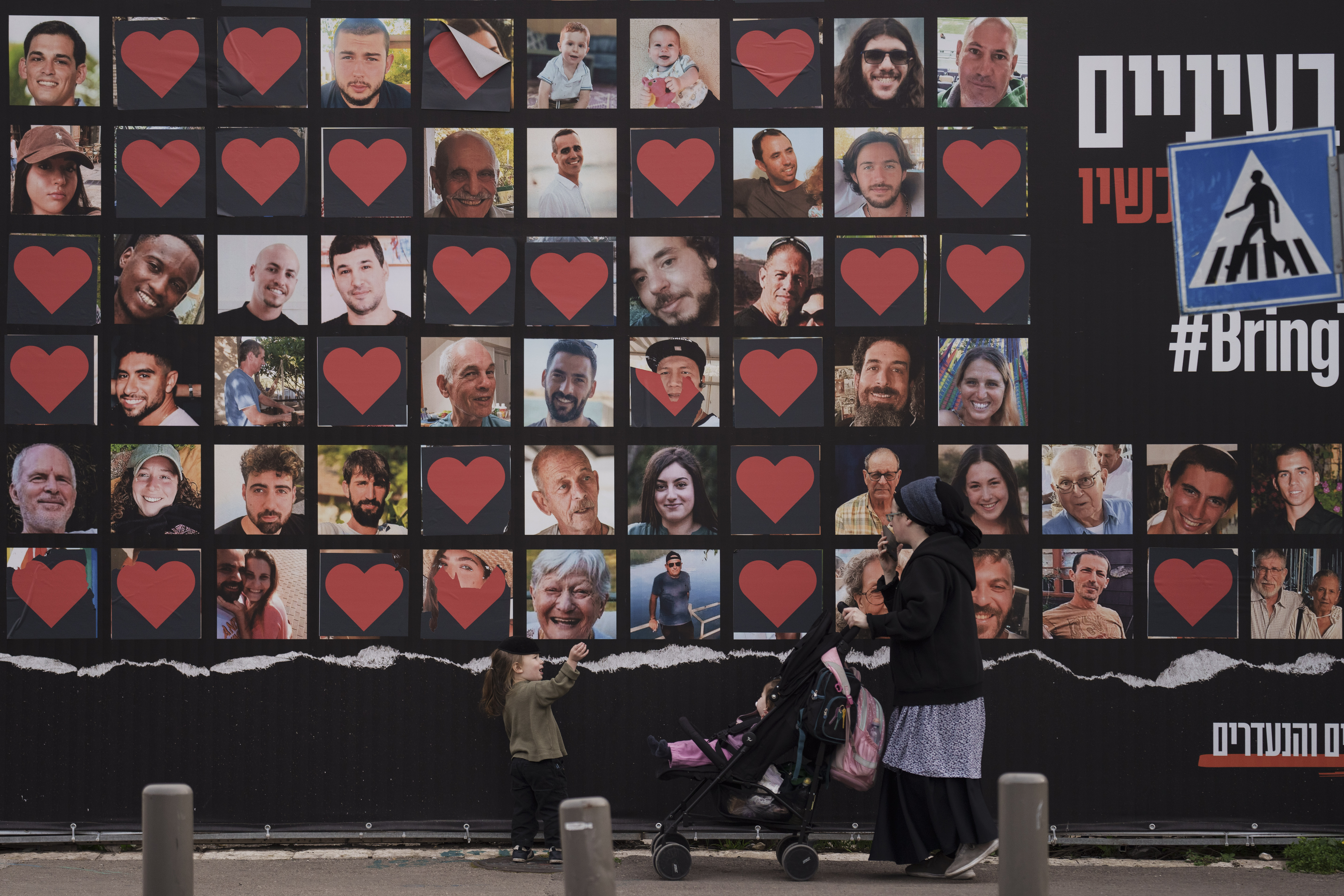 A woman and her children walk past a wall with photographs of hostages who were kidnapped during the October 7 cross-border attack led by Hamas in Israel. Photo / AP