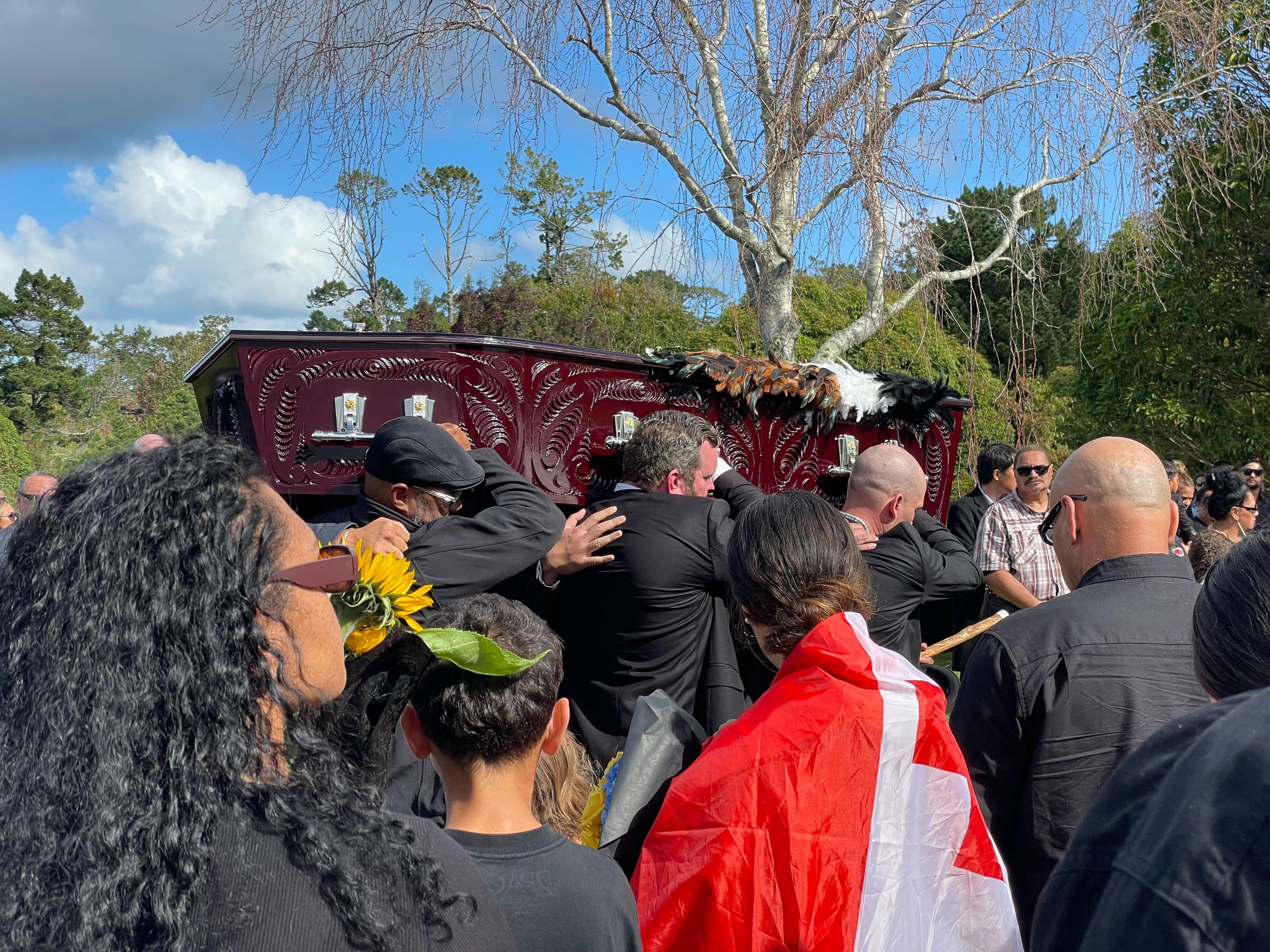 Kane Te Tai being led out at Waikumete Cemetery, as whānau follow behind with flowers. Photo / Candice Luke