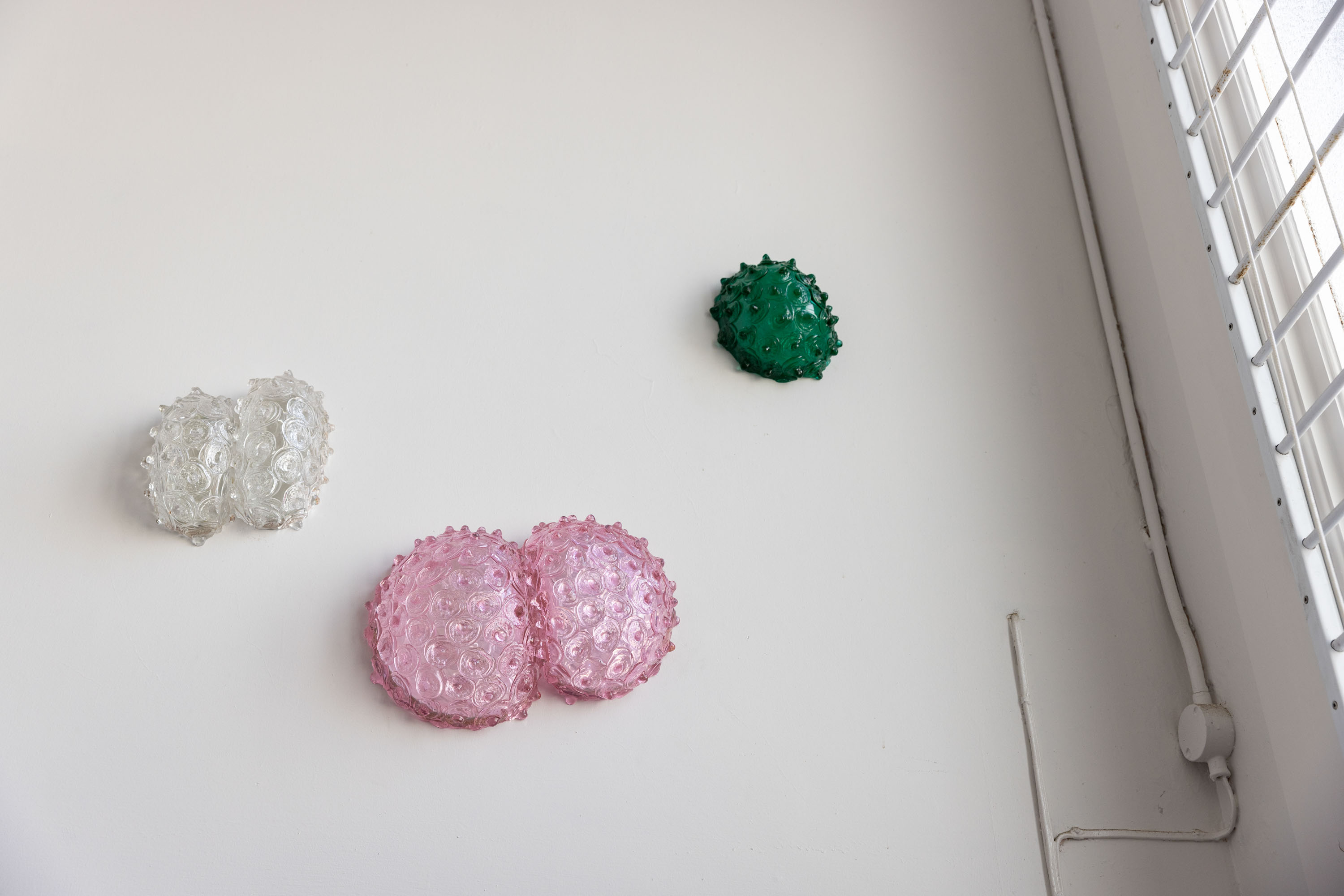 On the studio walls hang Double Bubble, blown and hot cast glass, mirror, birchwood ply, 230 x 250 x 140mm, 2016; Pink Double Bubble, blown and hot cast Erbium glass, mirror, birchwood ply, 250 x 370 x 140mm, 2016; and Green Merletto Bubble, blown and hot cast green uranium glass, mirror, birchwood ply, 200 x 240 x 130mm, 2016. Photo / Babiche Martens
