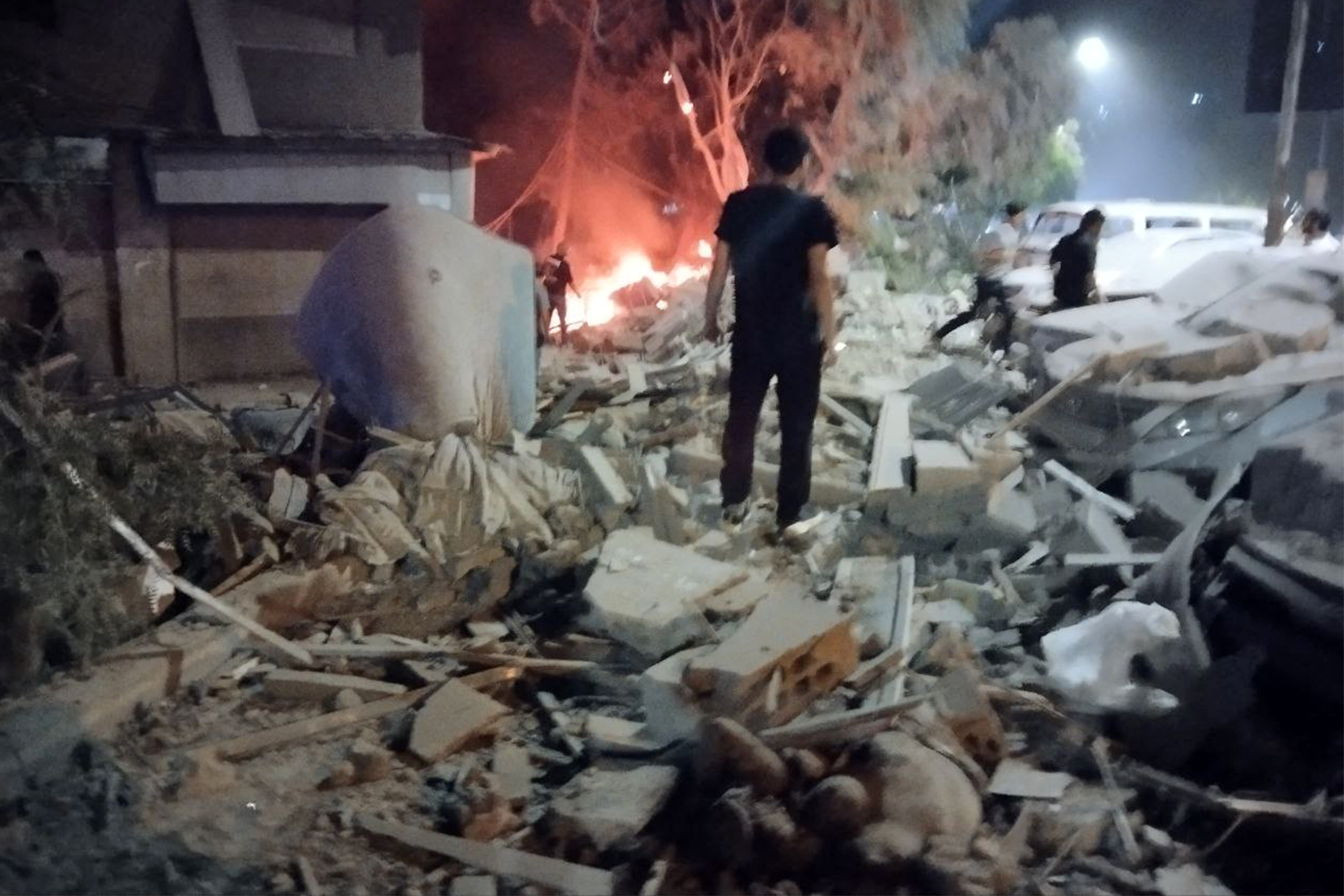 People gather by damaged vehicles at the site of a reported Israeli air strike on a residential building. Photo / AFP