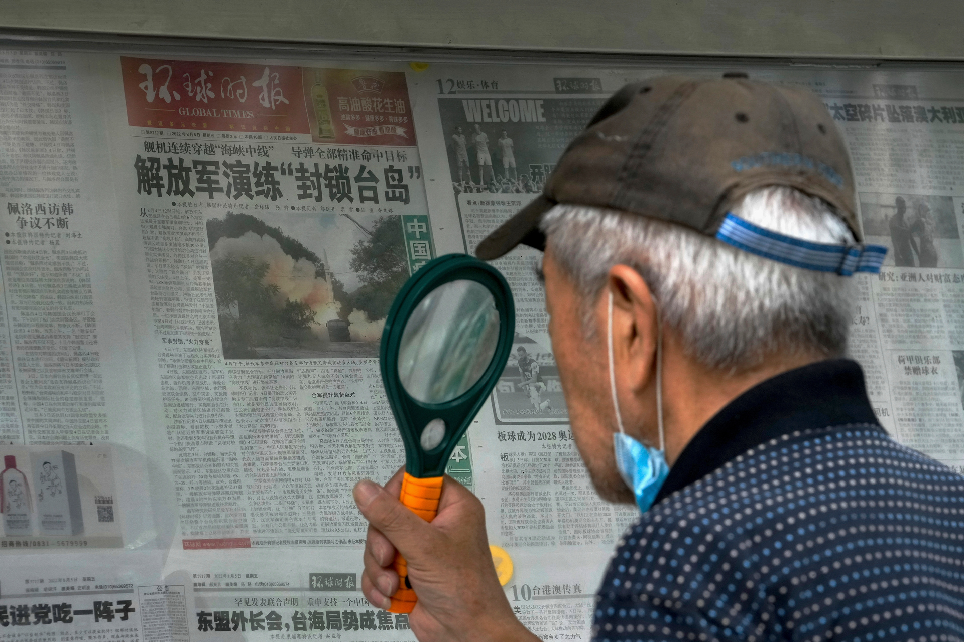 A man uses a magnifying glass to read a newspaper headline reporting on Chinese military exercises, at a stand in Beijing. Photo / Andy Wong, AP