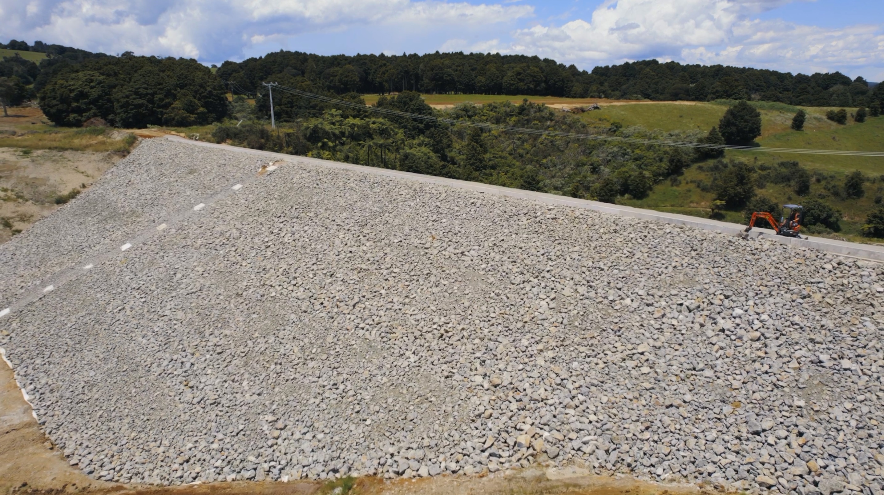 A digger is dwarfed by the inner face of Matawii Dam, near Kaikohe. Photo / Kānoa, MBIE