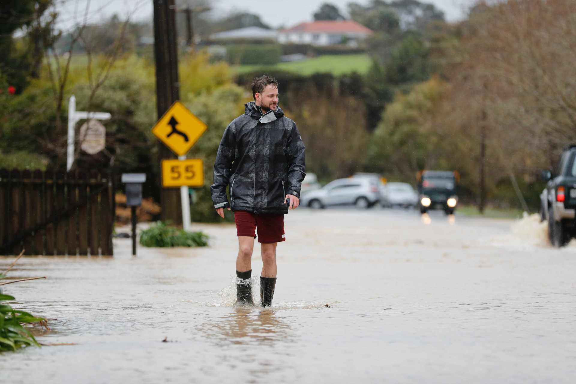 Ryan Jones wading through flood water on Taupaki Road. Photo / Dean Purcell
