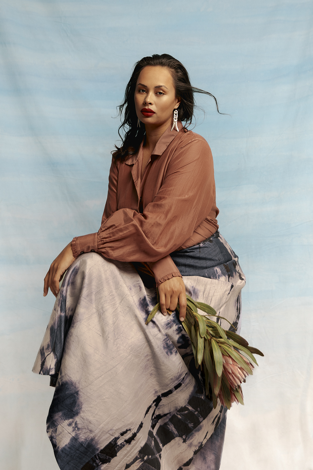The dusky terrains of Northern Australia give bloom to a collection of hardy flowers as featured in ‘The Lost Flowers of Alice Hart’, from the pendulous Sturt’s desert pea to the classic protea, their sunkissed colours inspire an awe-inspiring palette. Mahsa shirt $380. Liz Mitchell shibori dyed silk skirt $1495. Mi Piaci boots $320. Earrings from Masterworks Gallery (POA). Photo / Hōhua Ropate Kurene