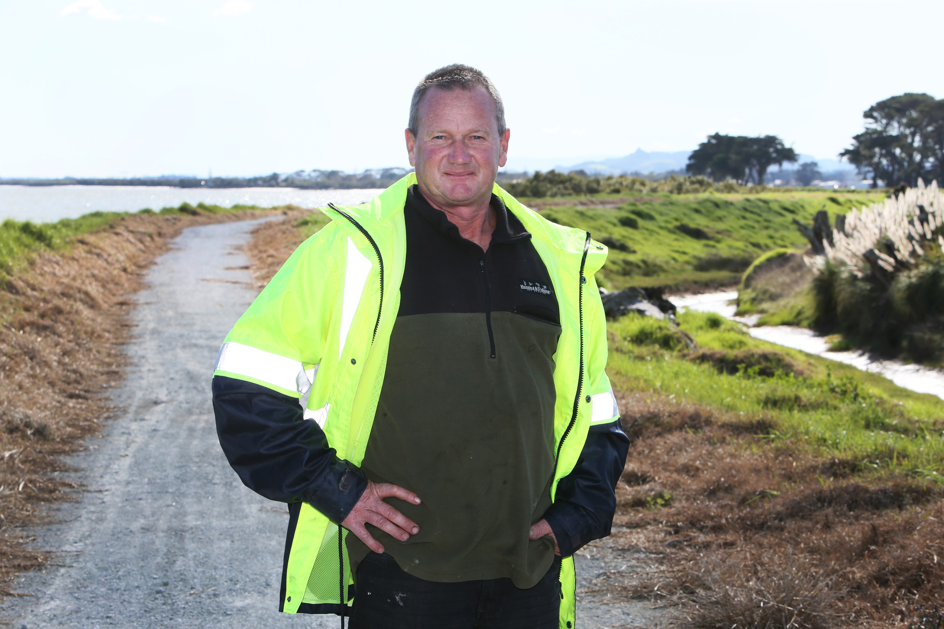 Raupo drainage committee chairman Ian Beattie atop scheme stopbanks holding back the Kaipara Harbour behind him.