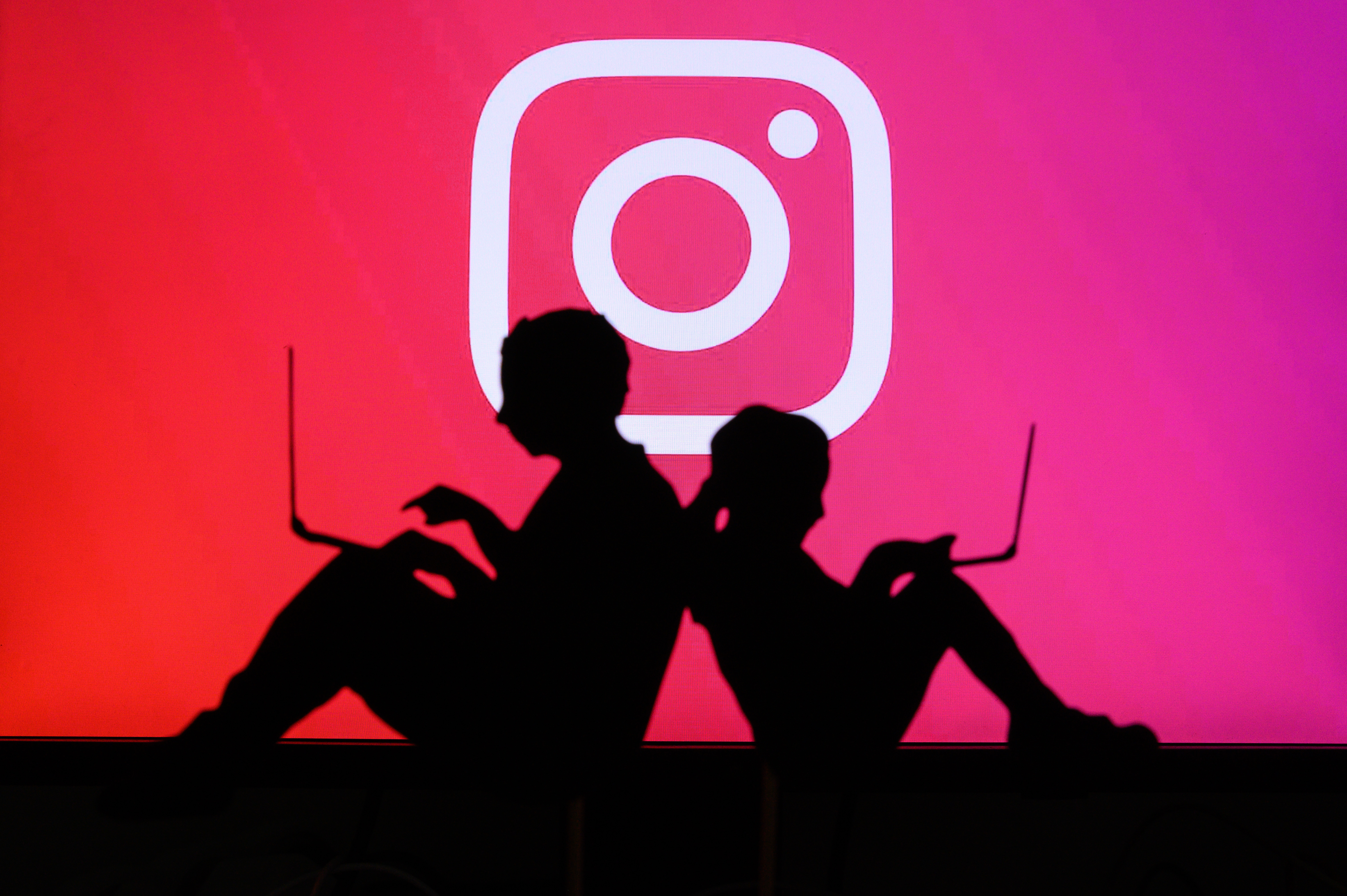 NEW YORK, USA, 25. MAY 2020: Instagram photo and video-sharing social networking service Children silhouette, sitting together and playing on their laptops. Company logo on screen in background