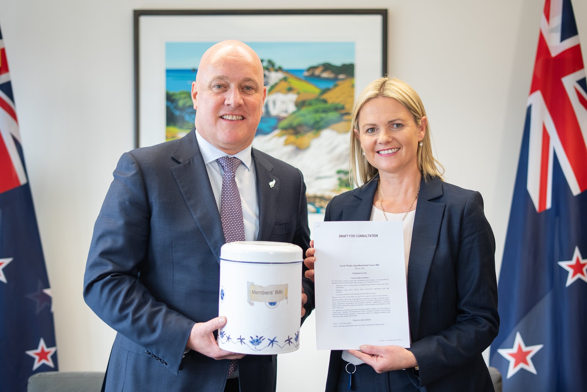 Tukituki MP Catherine Wedd with her bill banning social media for under 16s. Prime Minister Christopher Luxon, who supports the bill, is holding the biscuit tin from where member's bills are drawn. 