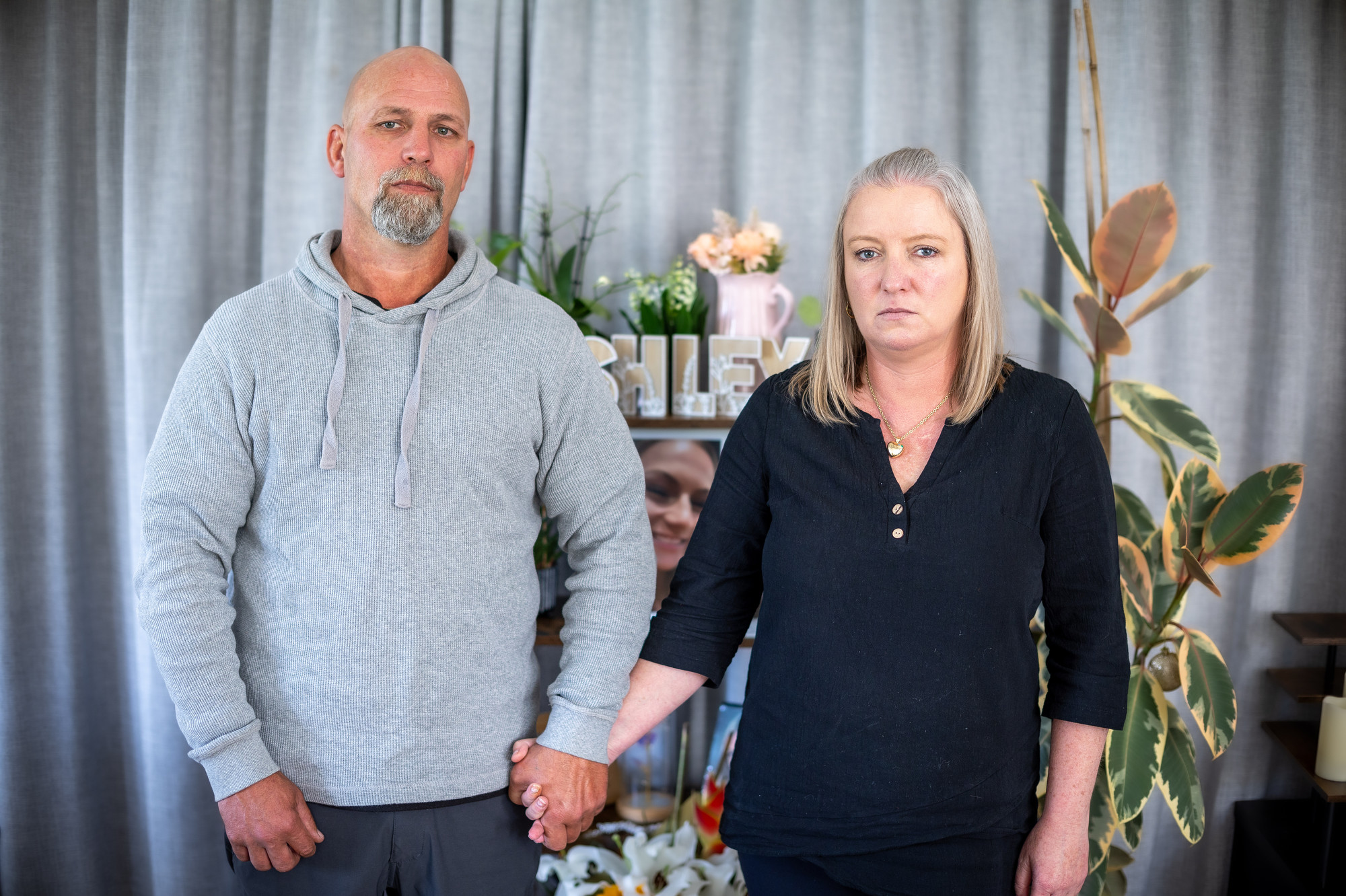 Gary and Danielle Wickman at their home in Hikurangi. The shelf behind carries photos of their daughter Ashley, who died in November 2024. Photo / Michael Craig
