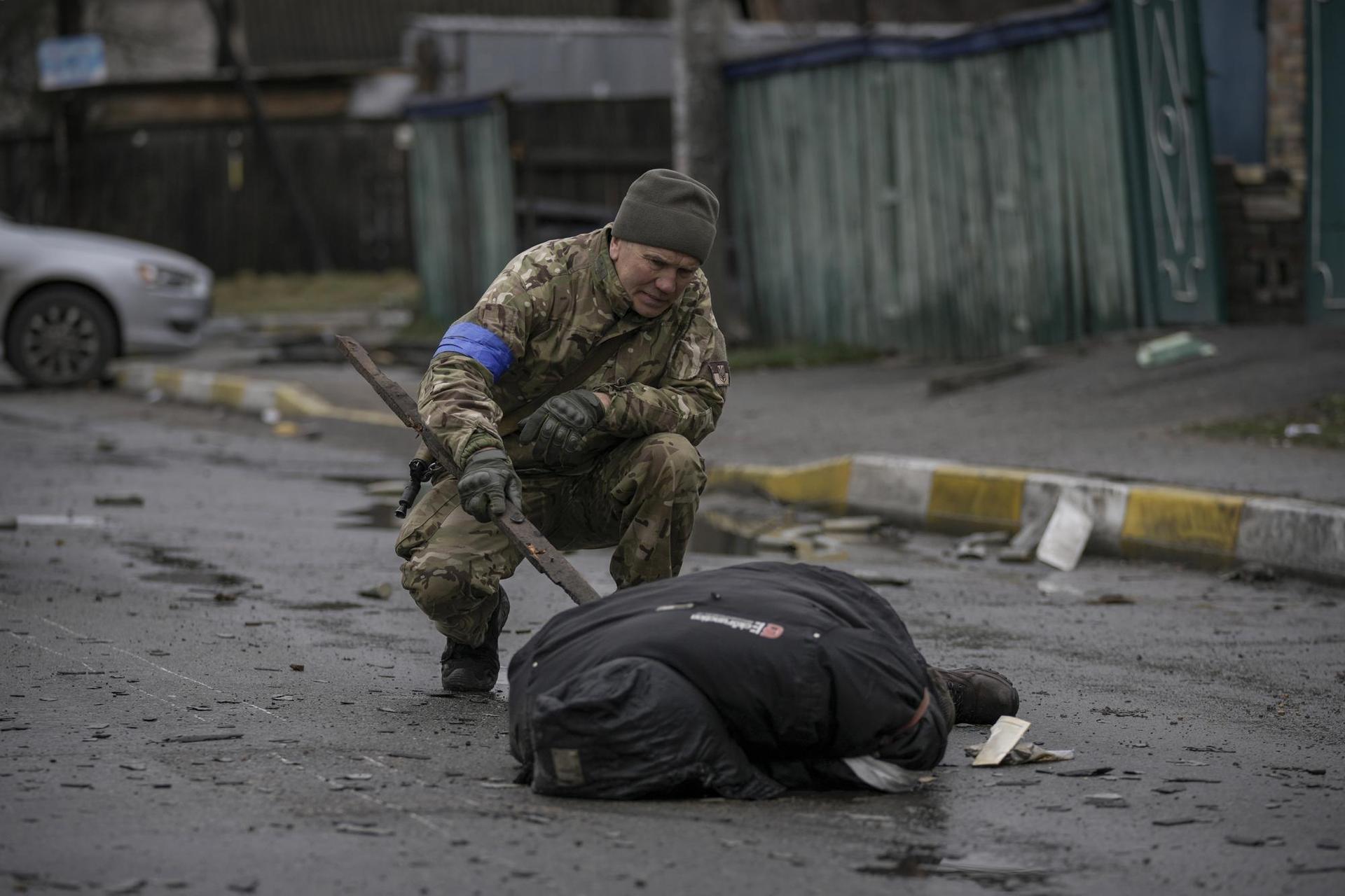 A Ukrainian serviceman uses a piece of wood to check if the body of a man dressed in civilian clothing is booby-trapped with explosive devices, in the Kyiv suburb of Bucha. Photo / AP
