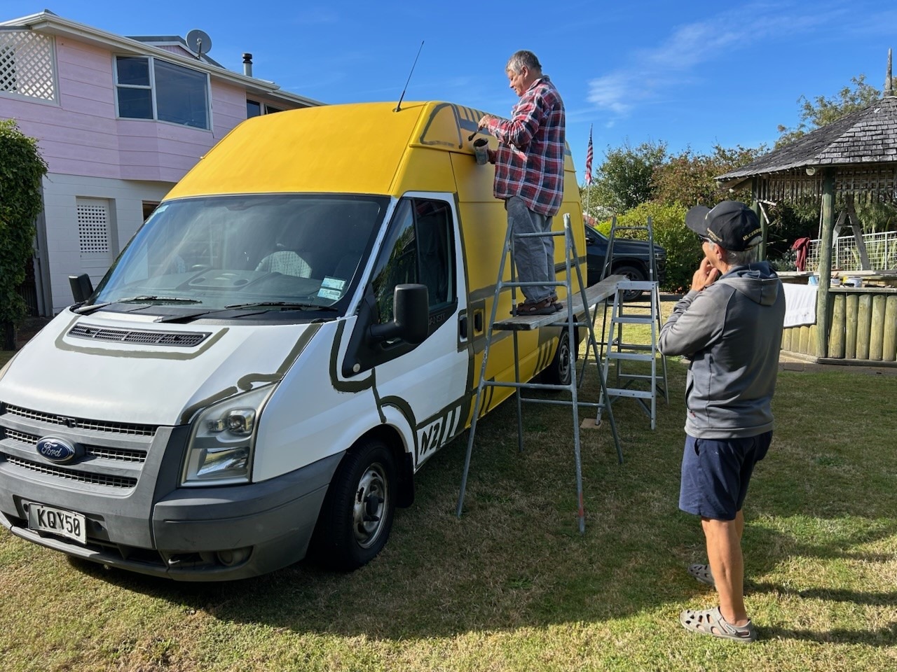 Artist Nigel Brown paints the hīkoi ambulance that will leave Kaitāia this week for Parliament. Watching is Dr Art Nahill who is on the hīkoi with GP Glenn Colquhoun.