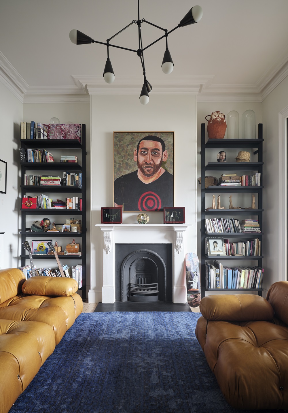 A painting of Tony Albert by Vincent Namatjira hangs above the fireplace and hand-carved greenstone pieces by Joe Sheehan are displayed on the mantelpiece. A large ceramic work by Claudia Nicholson sits on top of the shelving unit on the right. On the shelves to the left, paintings and a photographic print by Tony Albert sit among the books. The skateboard leaning against the wall is by Rakai Karaitiana.