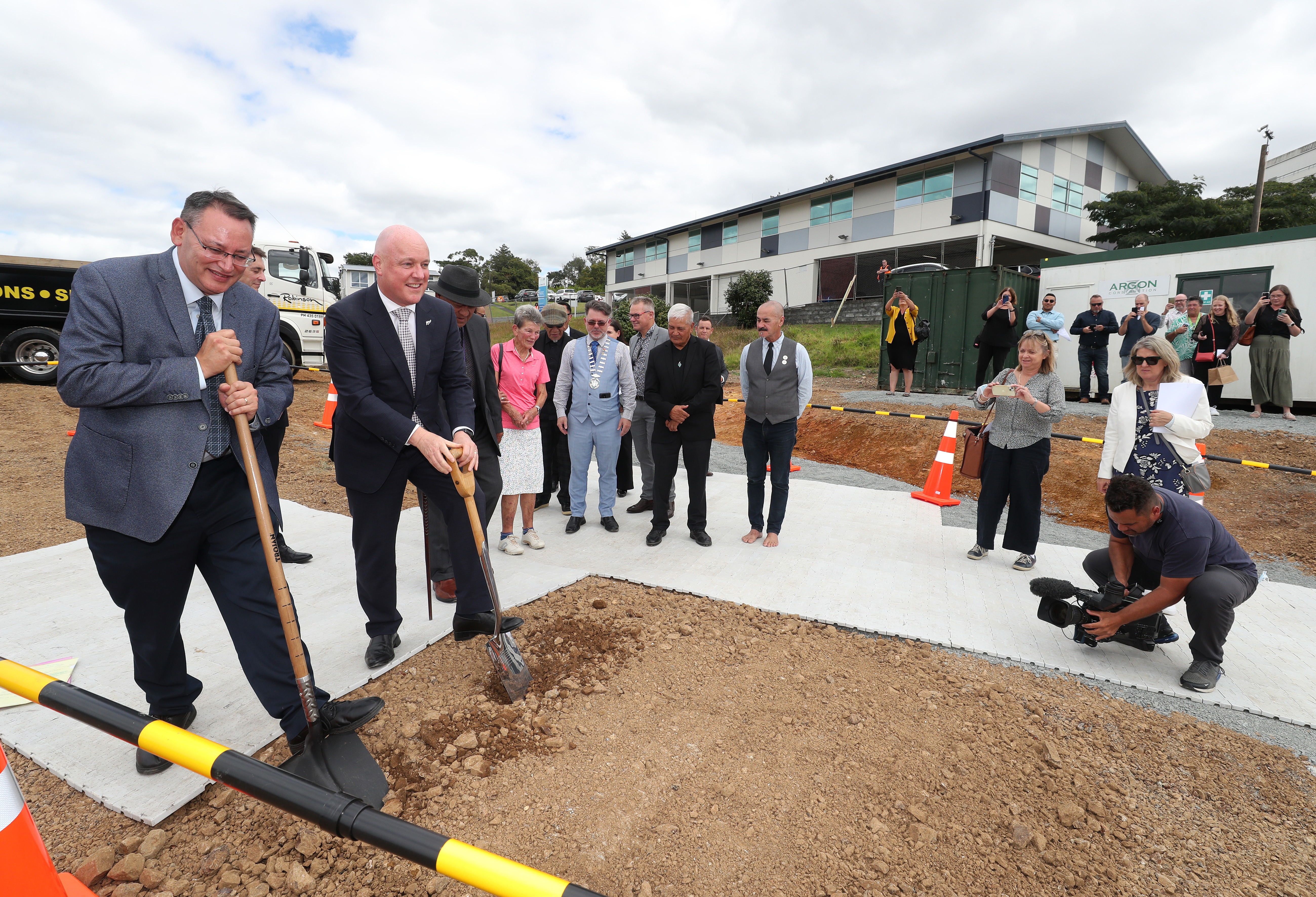 Dr Shane Reti and Christopher Luxon turn the first sod on the radiation facility in Whangārei watched by Mary Carney, wife of the late Jim Carney who the cancer facility is named after. Photo / Michael Cunningham