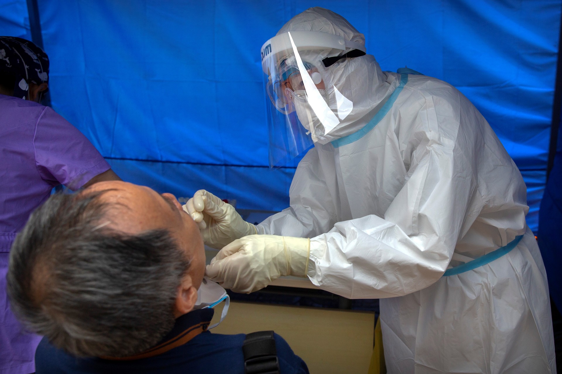 A worker wearing a protective suit swabs a man's throat for a coronavirus test at a community health clinic in Beijing. (AP Photo/Mark Schiefelbein)