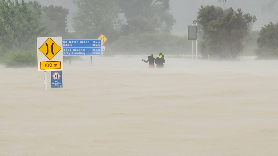 Two people wade through waist-high water after abandoning their car on the road to Hahei on the Coromandel Peninsula. PICTURE / MATTHEW DAVISON