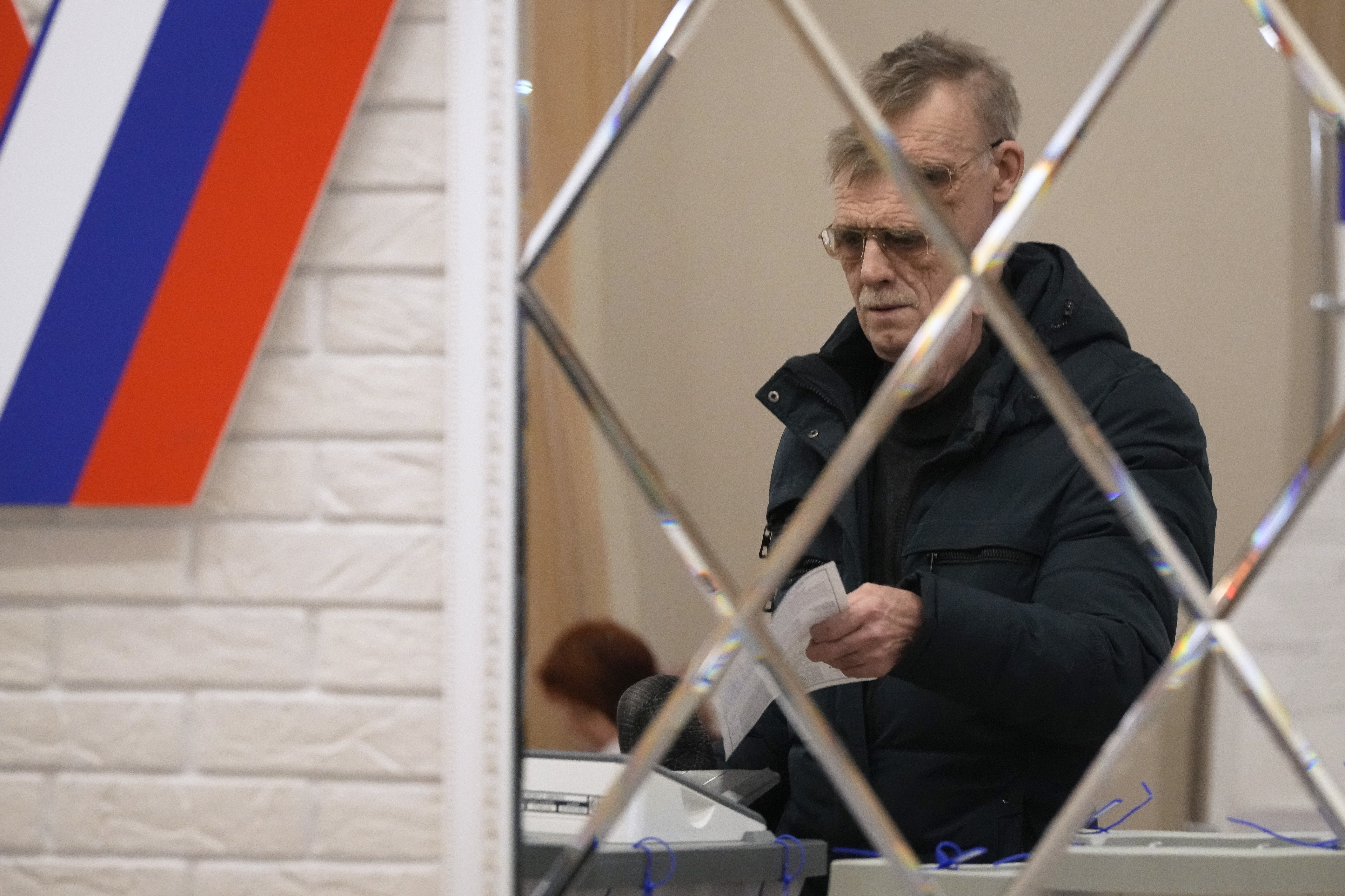 A man is reflected in a mirror as he casts a ballot at a polling station during the presidential elections in St Petersburg. Photo / AP