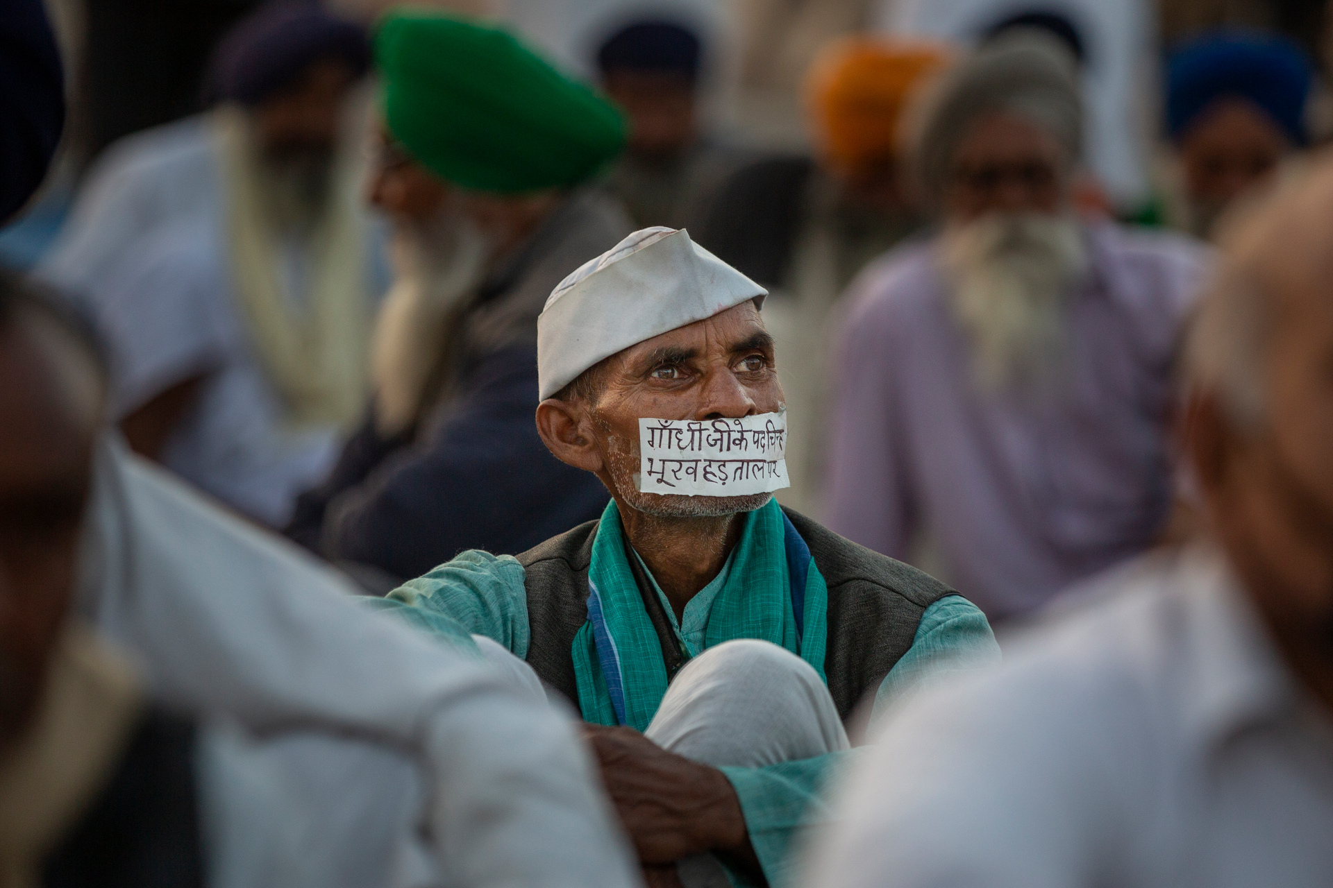 A farmer sits with a tape across his mouth that reads,