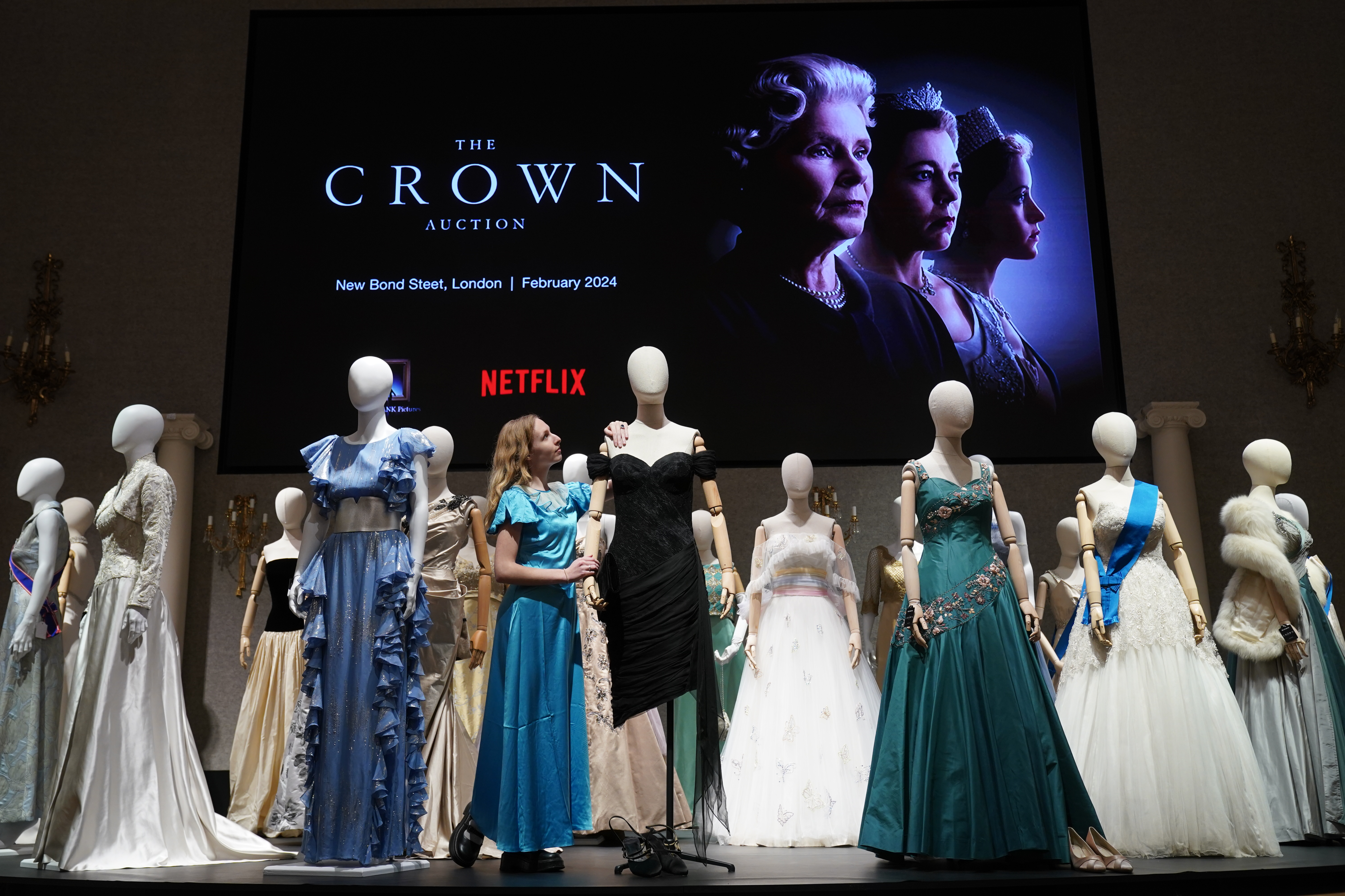 A gallery assistant adjusts a reproduction of Princess Diana's revenge dress to be auctioned  with more than 450 costumes, sets and props from the Netflix series The Crown. Photo / Lucy North - PA Images