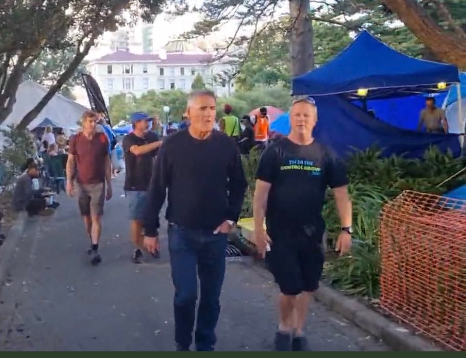 Sir Russell Coutts is escorted around the anti-mandate occupation protest site outside Parliament. Photo / via Richard Hills, Twitter 