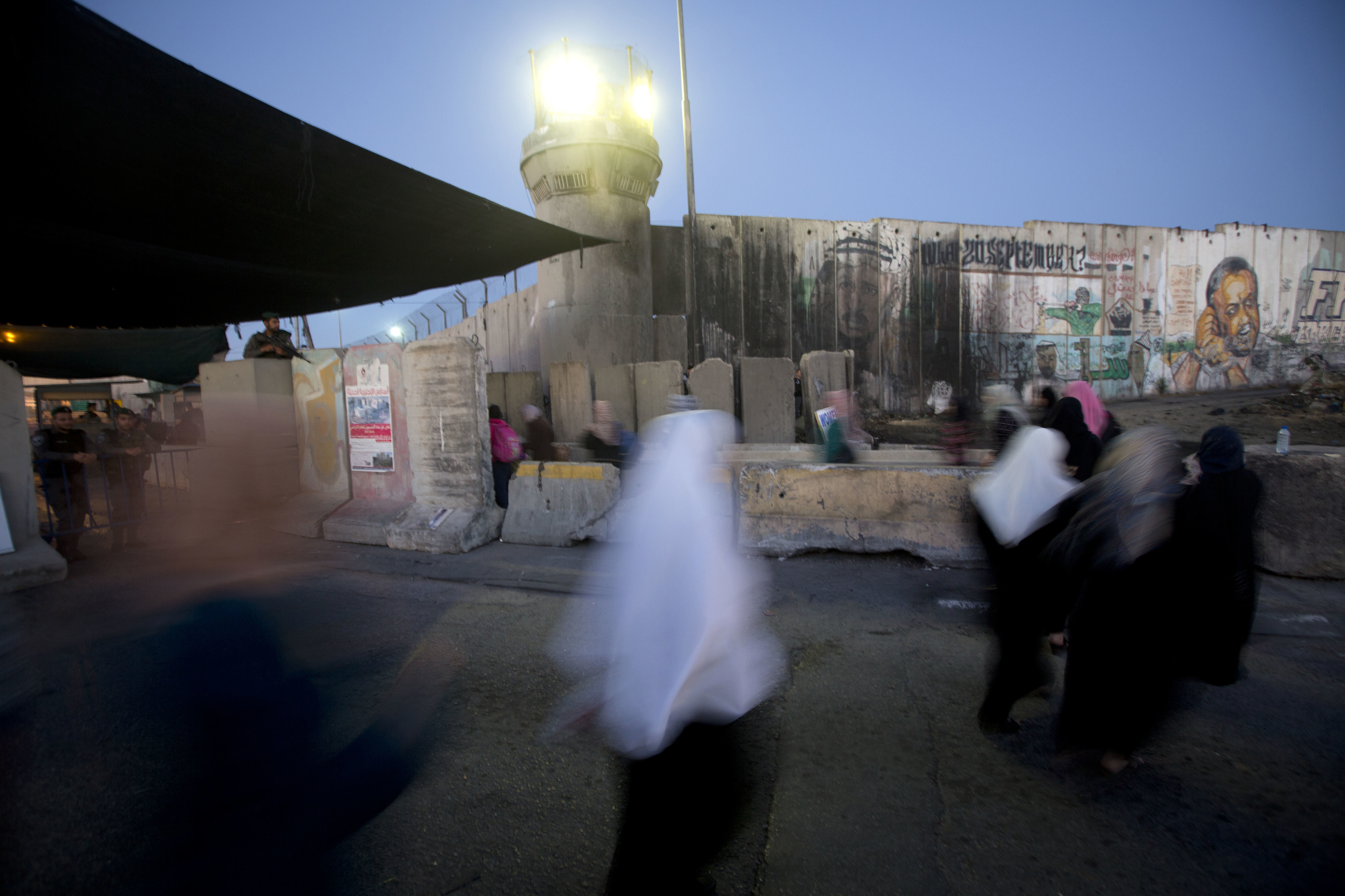 Palestinian women walk past a section of Israel's separation barrier to cross the Qalandia checkpoint between the West Bank city of Ramallah and Jerusalem.