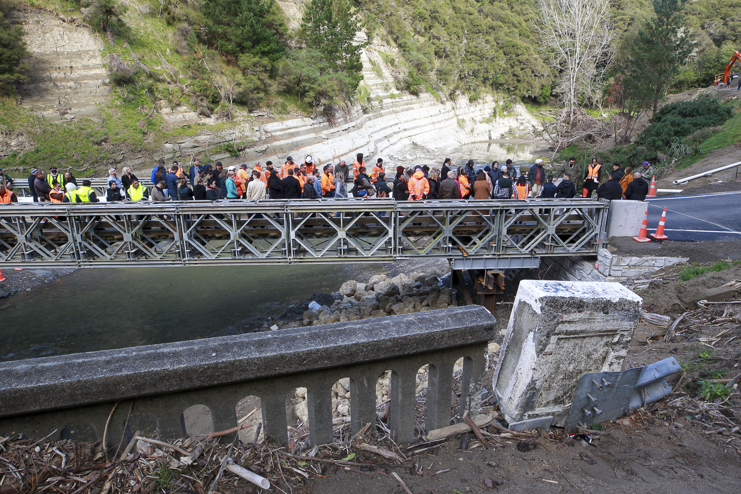 The destroyed Waikare River bridge (foreground) and the new Bailey bridge and the gathering at its blessing on Saturday. Photo / Paul Taylor