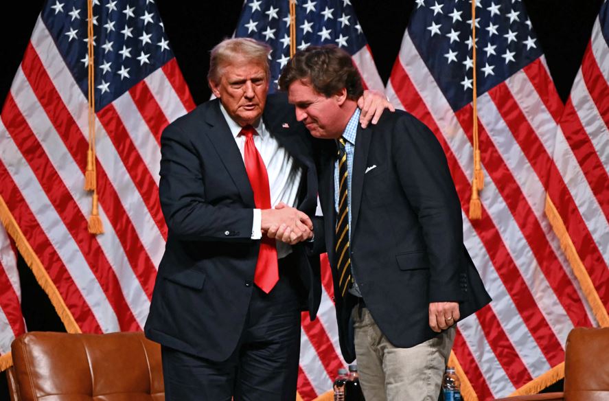 Former US President and Republican presidential candidate Donald Trump (L) shakes hands with US commentator Tucker Carlson at the end of a live interview in the finale of the Tucker Carlson Live Tour at Desert Diamond Arena in Glendale, Arizona, on October 31, 2024. (Photo by Patrick T. Fallon / AFP)