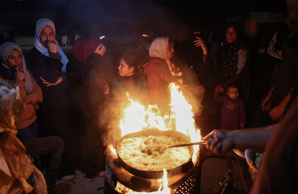 People wait for a hot meal at a food stall in a makeshift displacement camp in Khan Yunis in southern Gaza. Photo / AFP