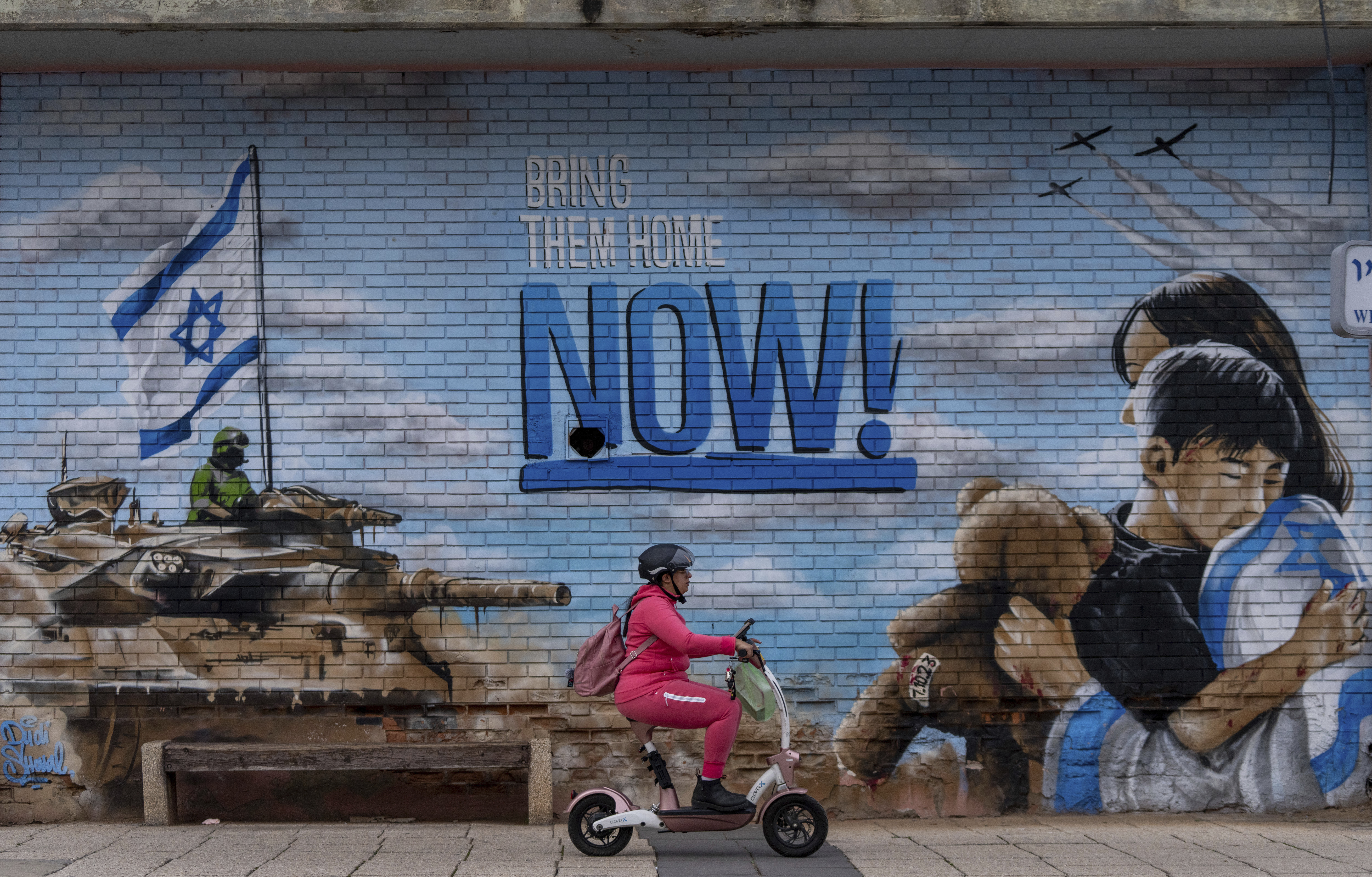 A woman rides a scooter past a graffiti calling for the return of the hostages kidnapped during the October 7 cross-border attack led by Hamas in Israel. Photo / AP