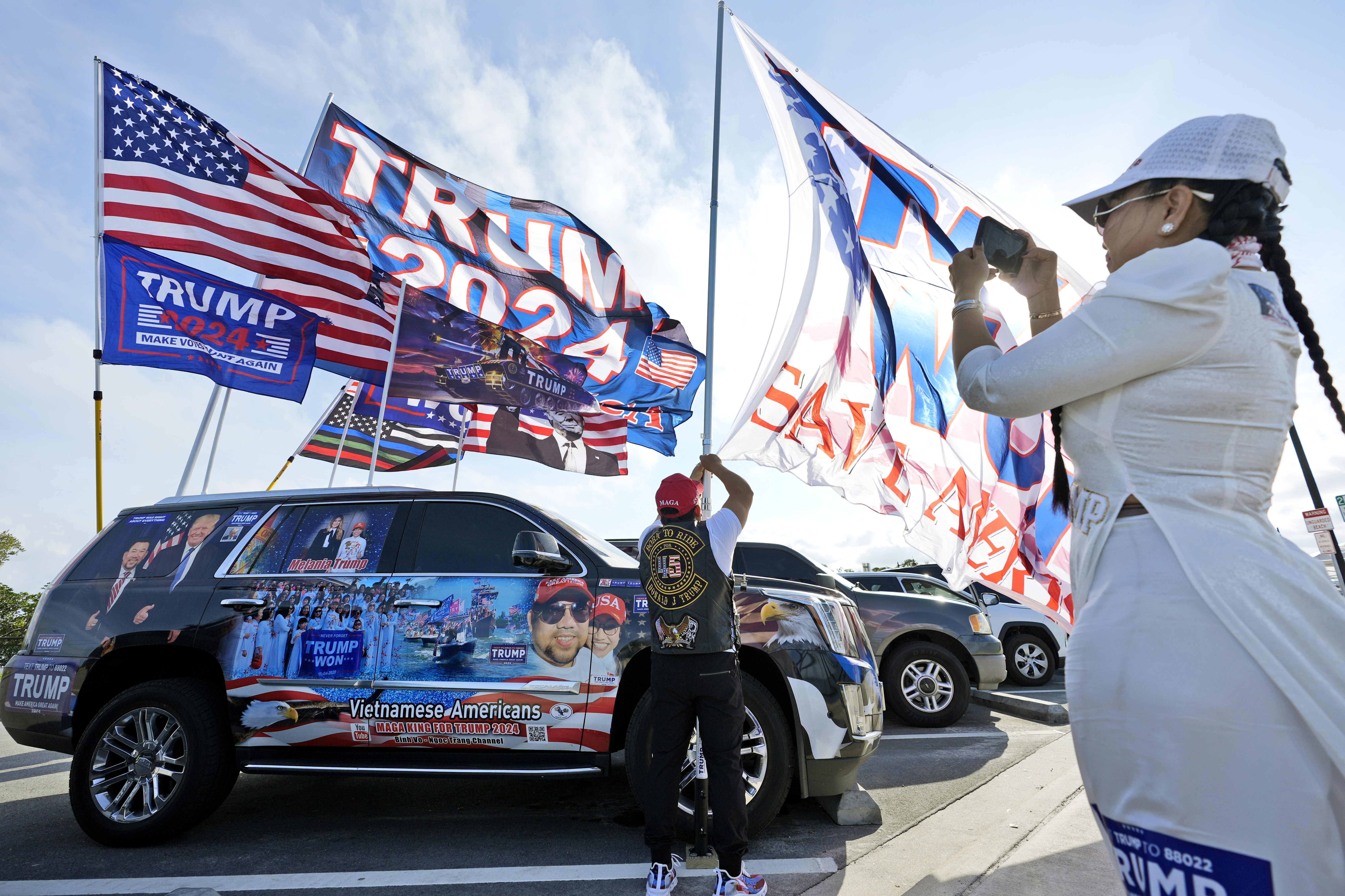 Binh Vo, rear, of Orlando, Florida, puts flags on his car as his wife Trang Ngoc, takes a video near Republican presidential candidate former President Donald Trump's Mar-a-Lago estate. Photo / AP