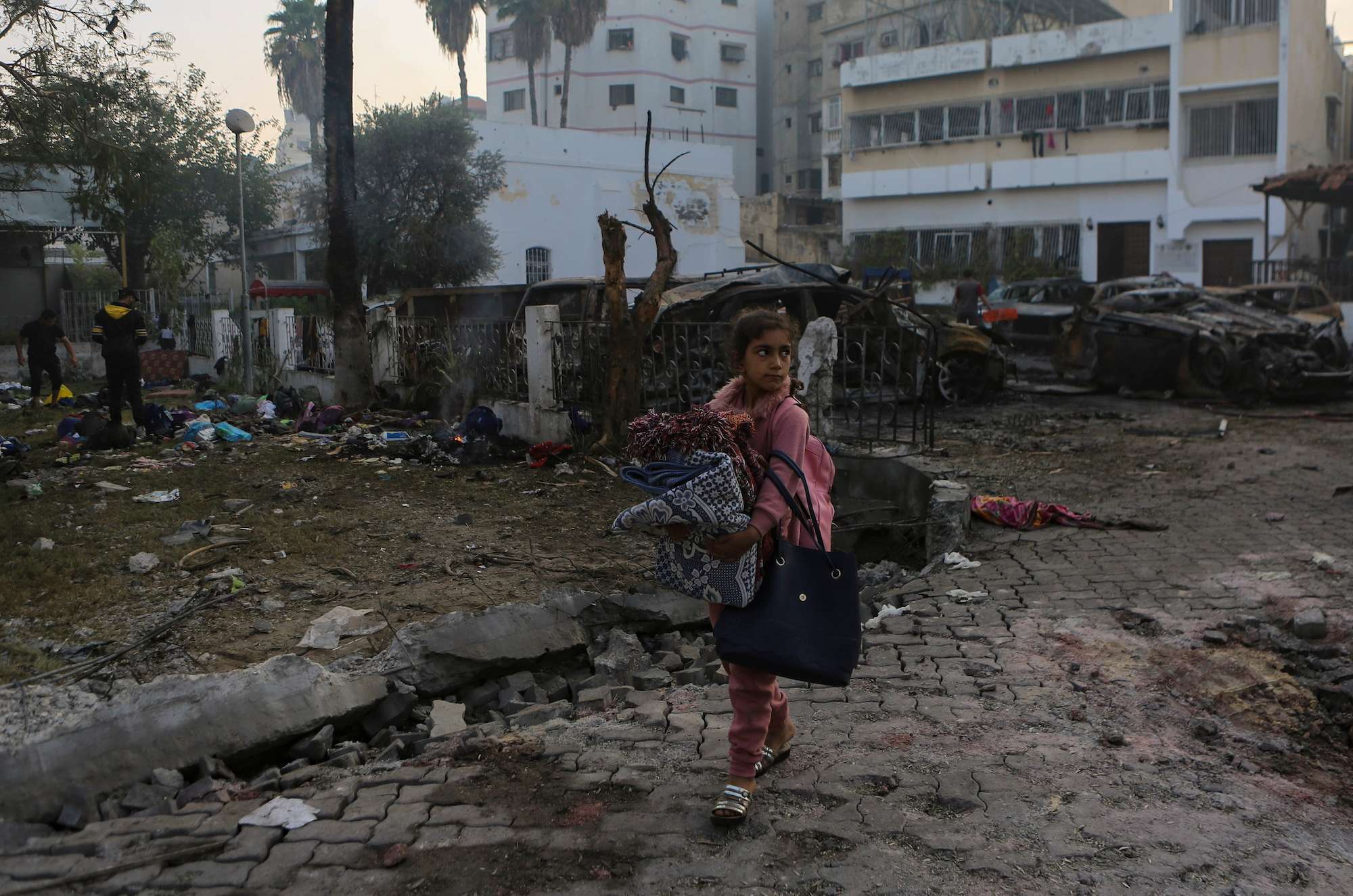 A Palestinian girl carries a blanket as she walks past the explosion scene at al-Ahli hospital, in Gaza City. Photo / AP