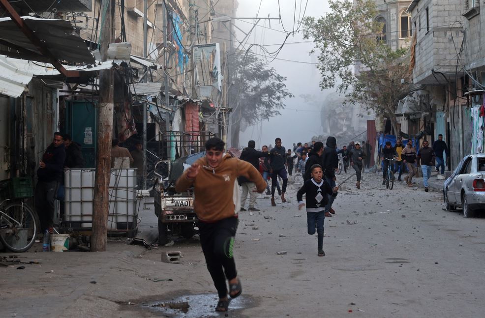 People run for cover as smoke rises from a building destroyed in Israeli airstrike at the Bureij camp for Palestinian refugees in the central Gaza Strip. Photo / AFP