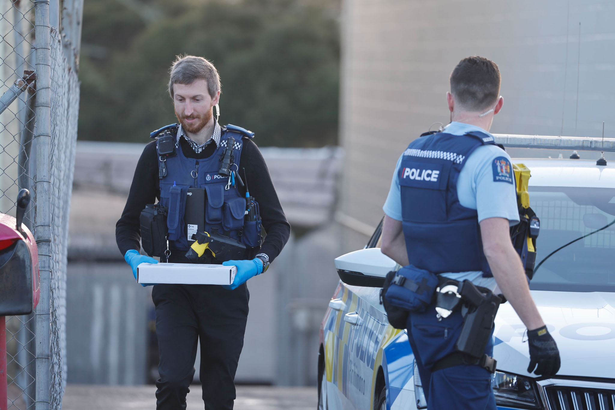 Three armed police officers were seen standing in front of the Head Hunters gang pad in West Auckland as an officer wearing blue gloves came out of the property carrying an evidence box. Photo / Michael Craig
