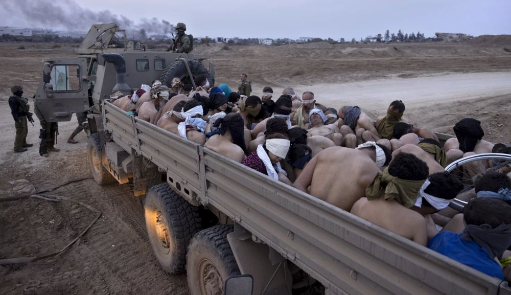 Israeli soldiers stand by a truck packed with bound and blindfolded Palestinian detainees. Photo / AP