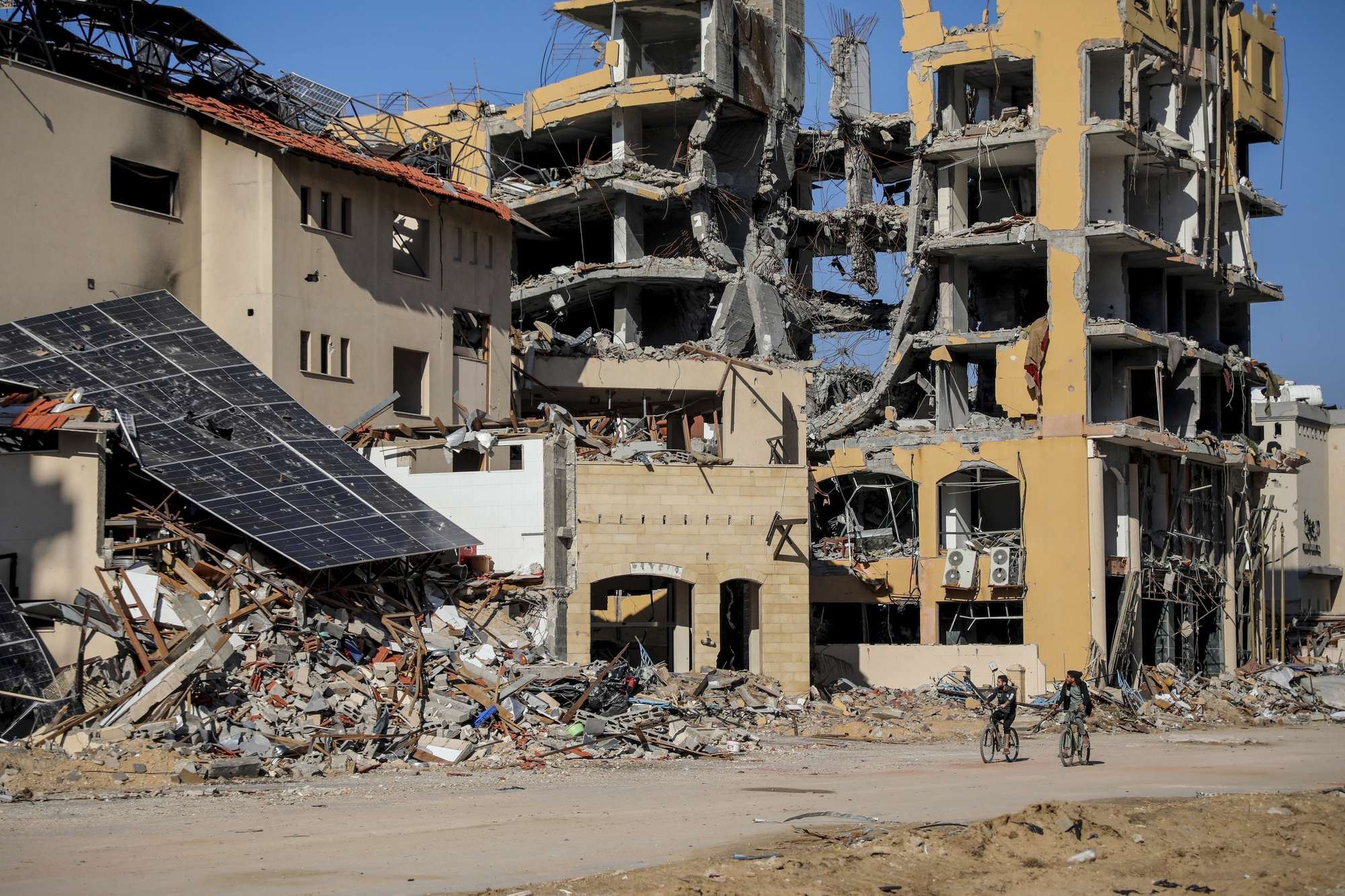 Palestinians ride bicycles by destroyed buildings in Gaza City. Photo / AP