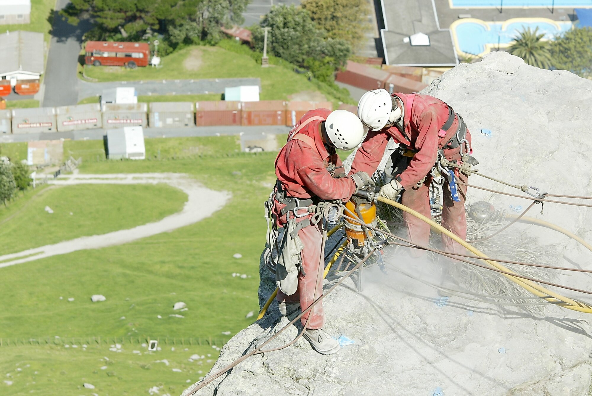 Avalon Industrial Services employees drill holes in the rock for explosives. Some of the 47 shipping containers used to protect the campsite and pools can be seen below. Photo / NZME