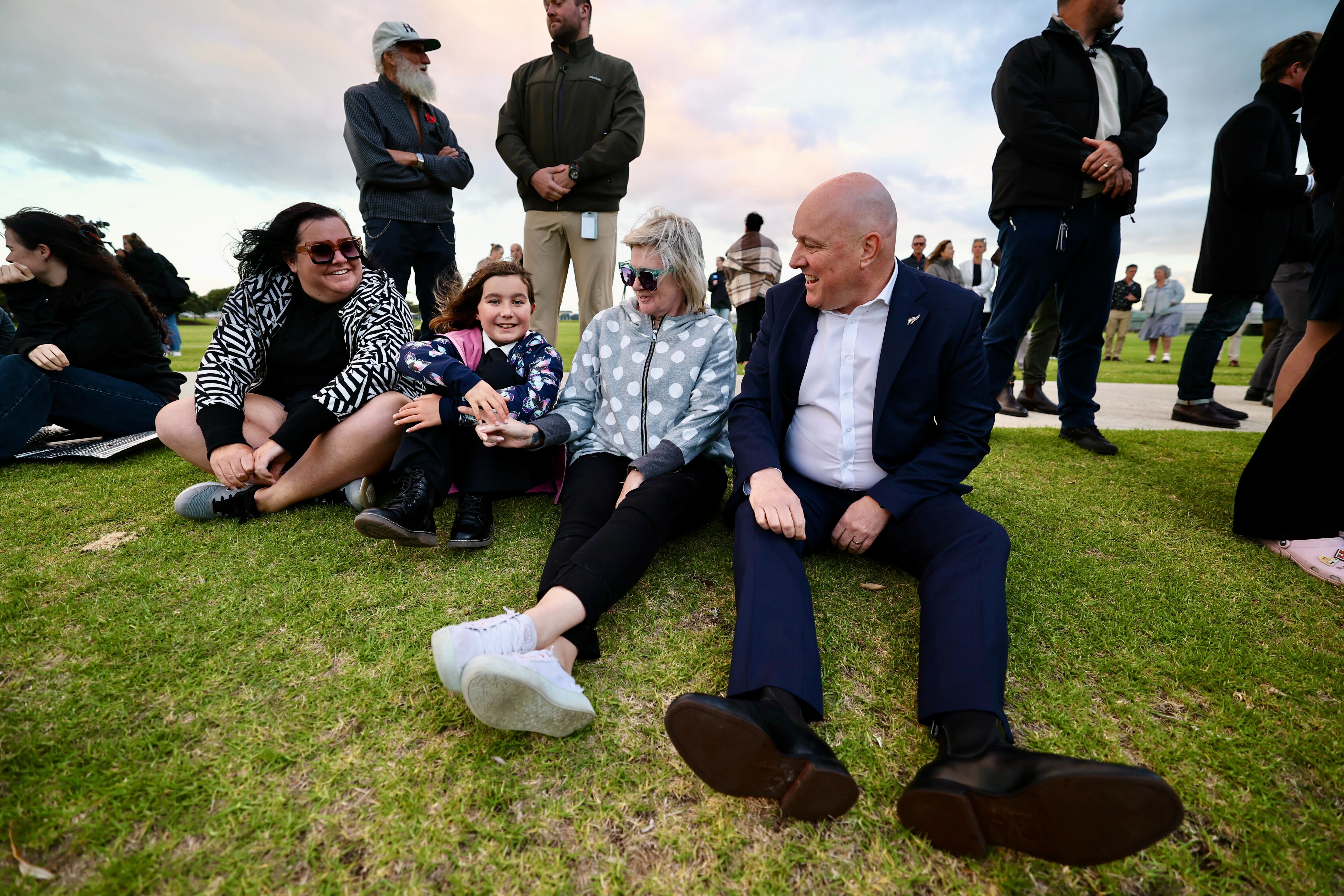 Prime Minister Christopher Luxon sits with people at a late-night vigil in Mount Maunganui. Photo / Dean Purcell 