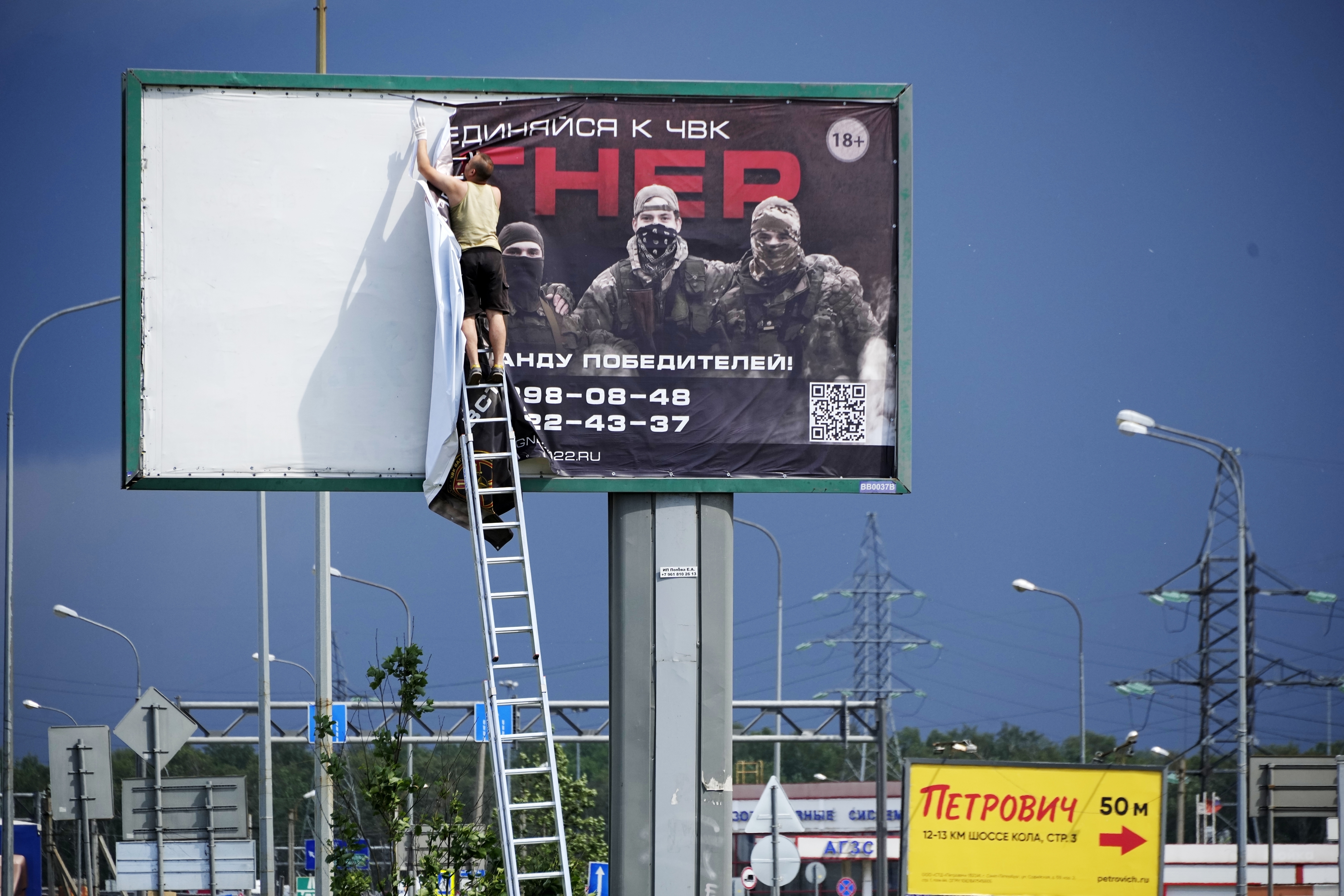 A man takes down the poster reading 'Join us at Wagner', on the outskirts of St. Petersburg, Russia. Photo / AP
