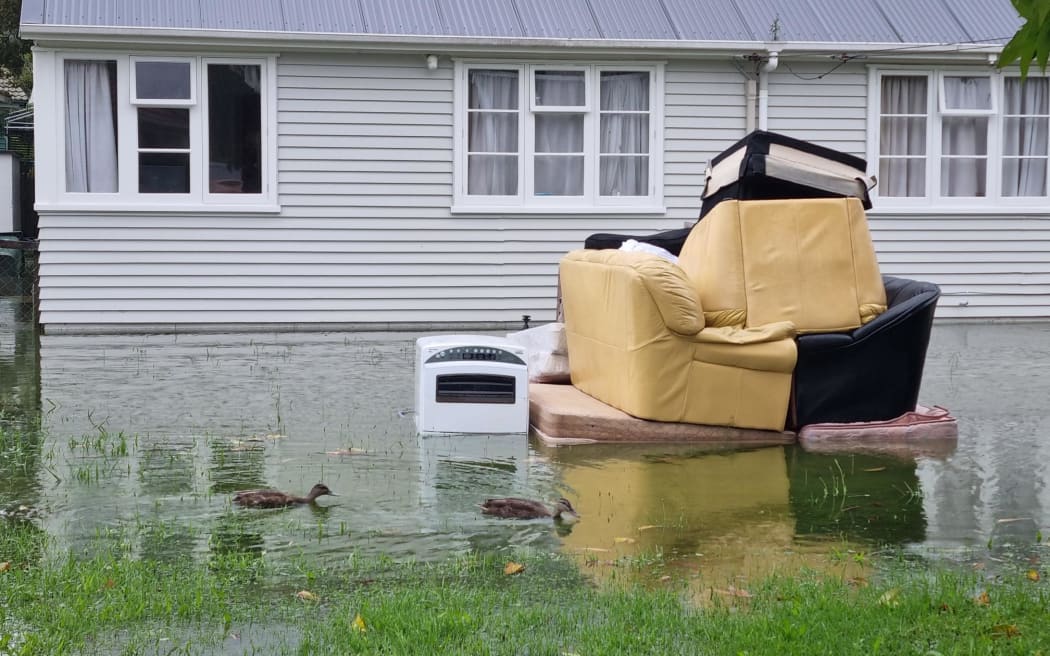 A house hit by flooding with damaged furniture piled up on a sodden lawn in the Auckland suburb of Mt Roskill. Photo / Rayssa Almeida / RNZ
