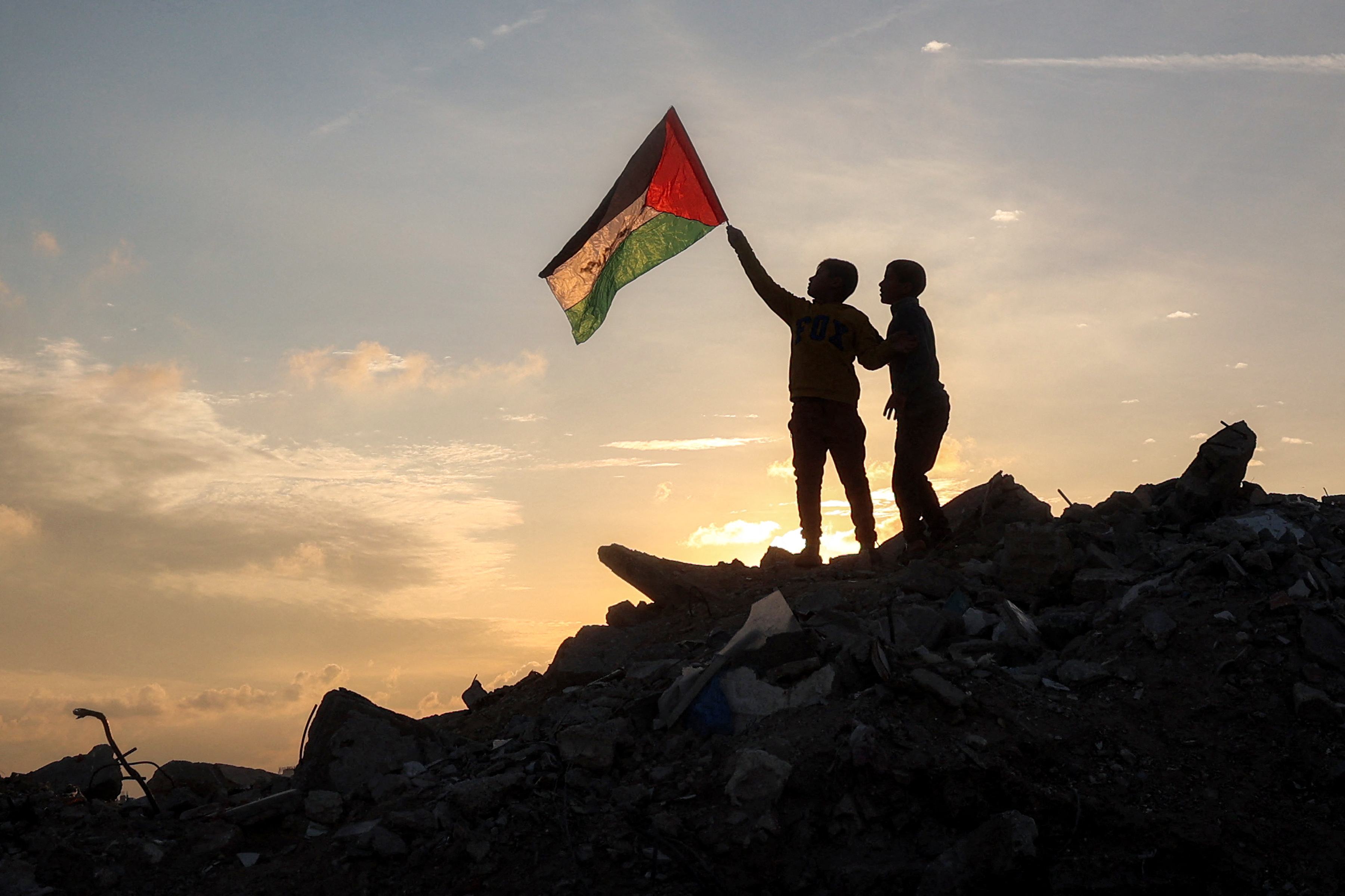 A boy waves a Palestinian flag atop a mound of rubble at a camp for people displaced by conflict in central Gaza after the announcement of a truce between Israel and Hamas. Photo / AFP