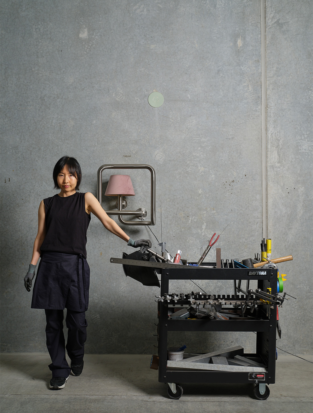 Sculptor Yona Lee bends and twists stainless steel tubing to collapse contexts and evoke emotion. Yona Lee, 2025, studio portrait, pictured with ‘Lamp in Transit’, 2025, Stainless steel, lamp, 48.5 x 46.5 x 33.5cm.
Courtesy the artist and Fine Arts, Sydney. Photo / Sam Hartnett
